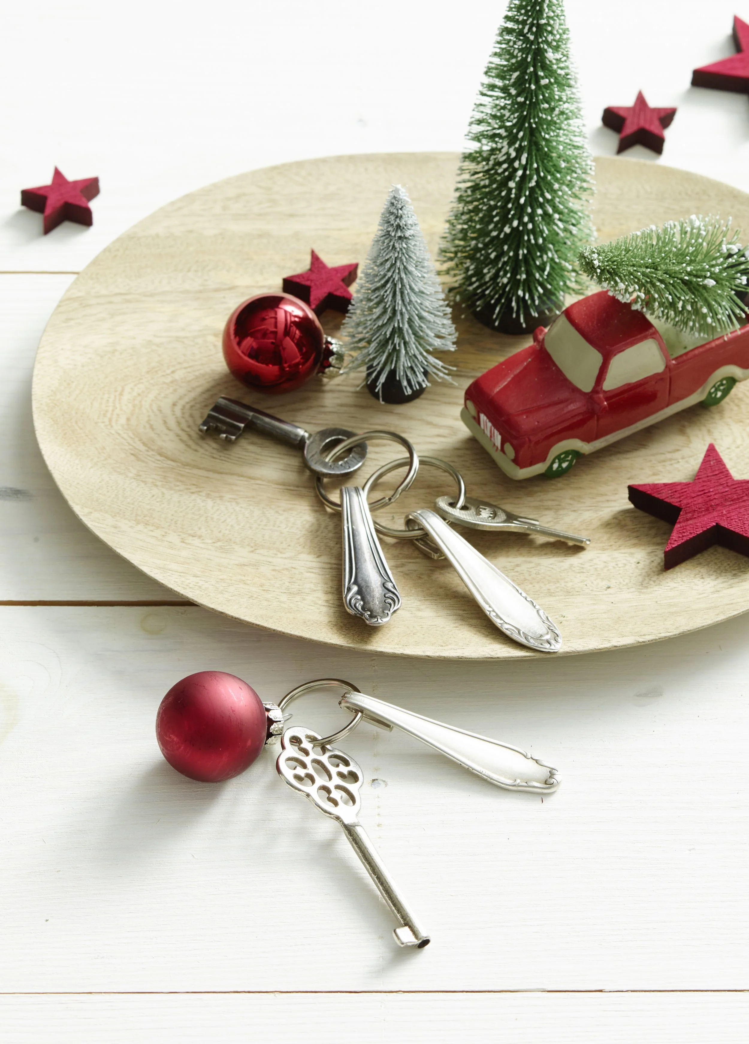 Weihnachtsdeko mit Mini-Tannenbäumen, roten Sternen, einer roten Weihnachtskugel, einem roten Auto und Schlüssel auf einem Holzplatte.