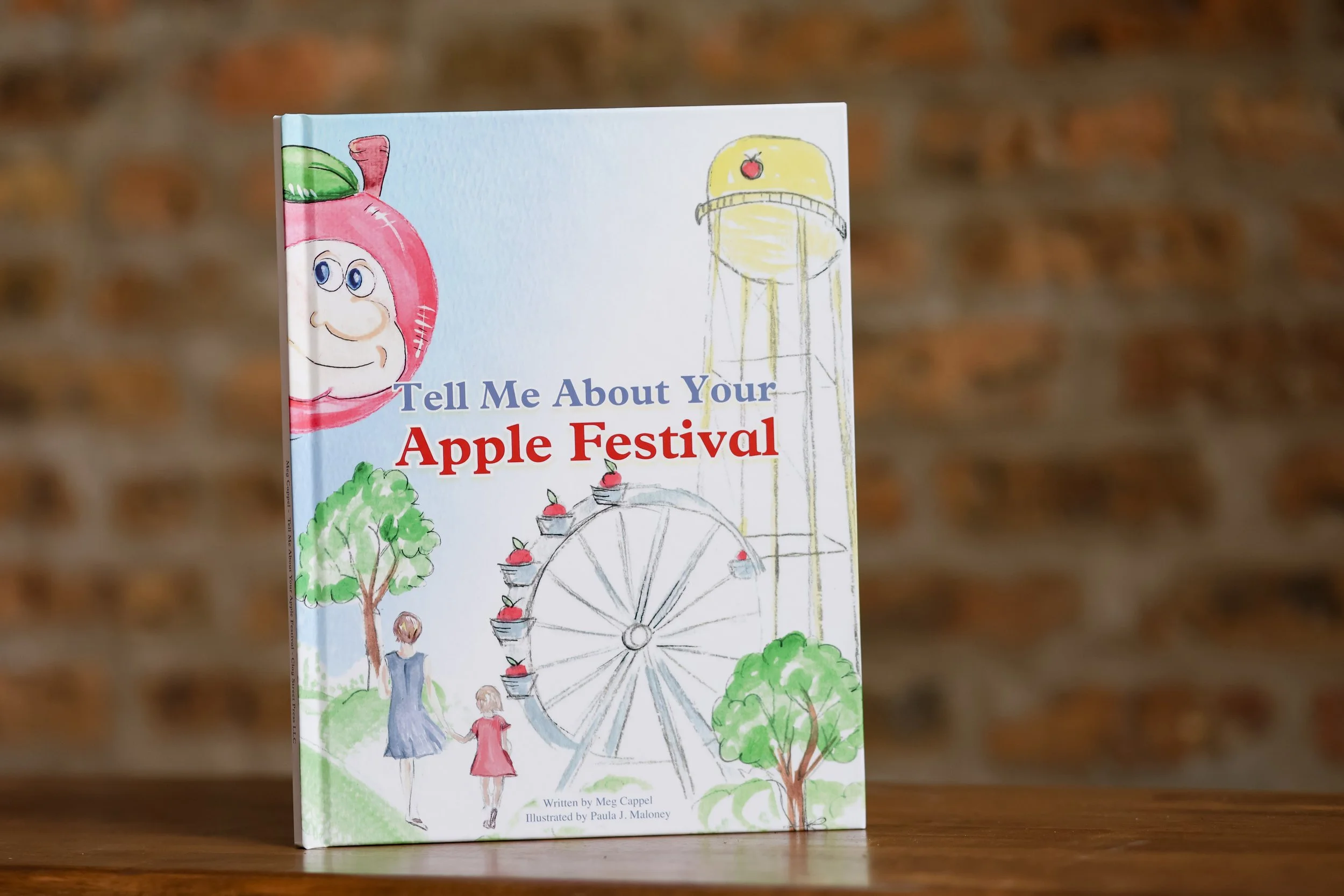 Children at an apple festival participating in activities with drawings of a smiling apple character, a Ferris wheel, and trees, on the cover of a book titled "Tell Me About Your Apple Festival."