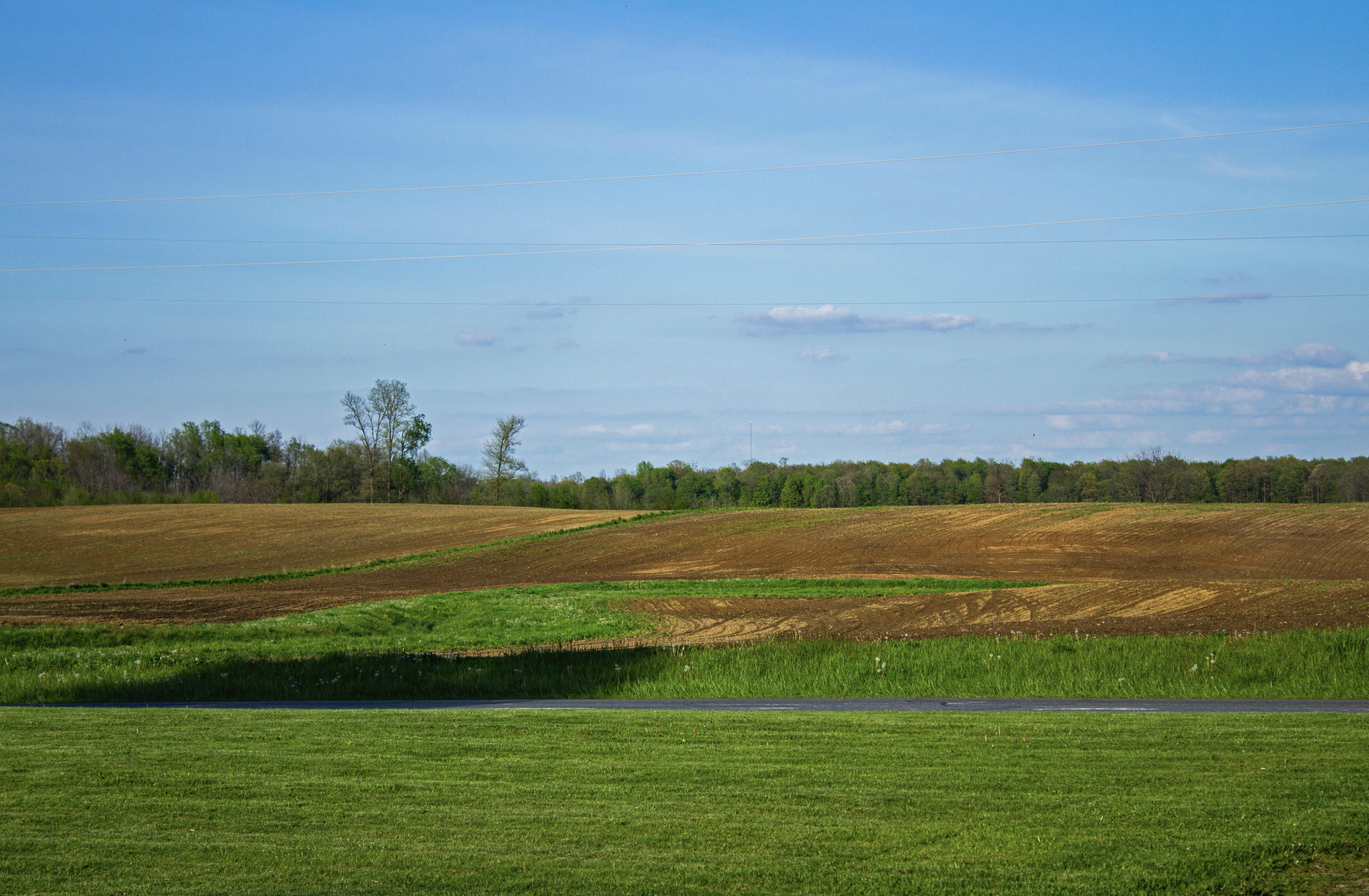 Open landscape with fields, trees, and a partly cloudy sky.