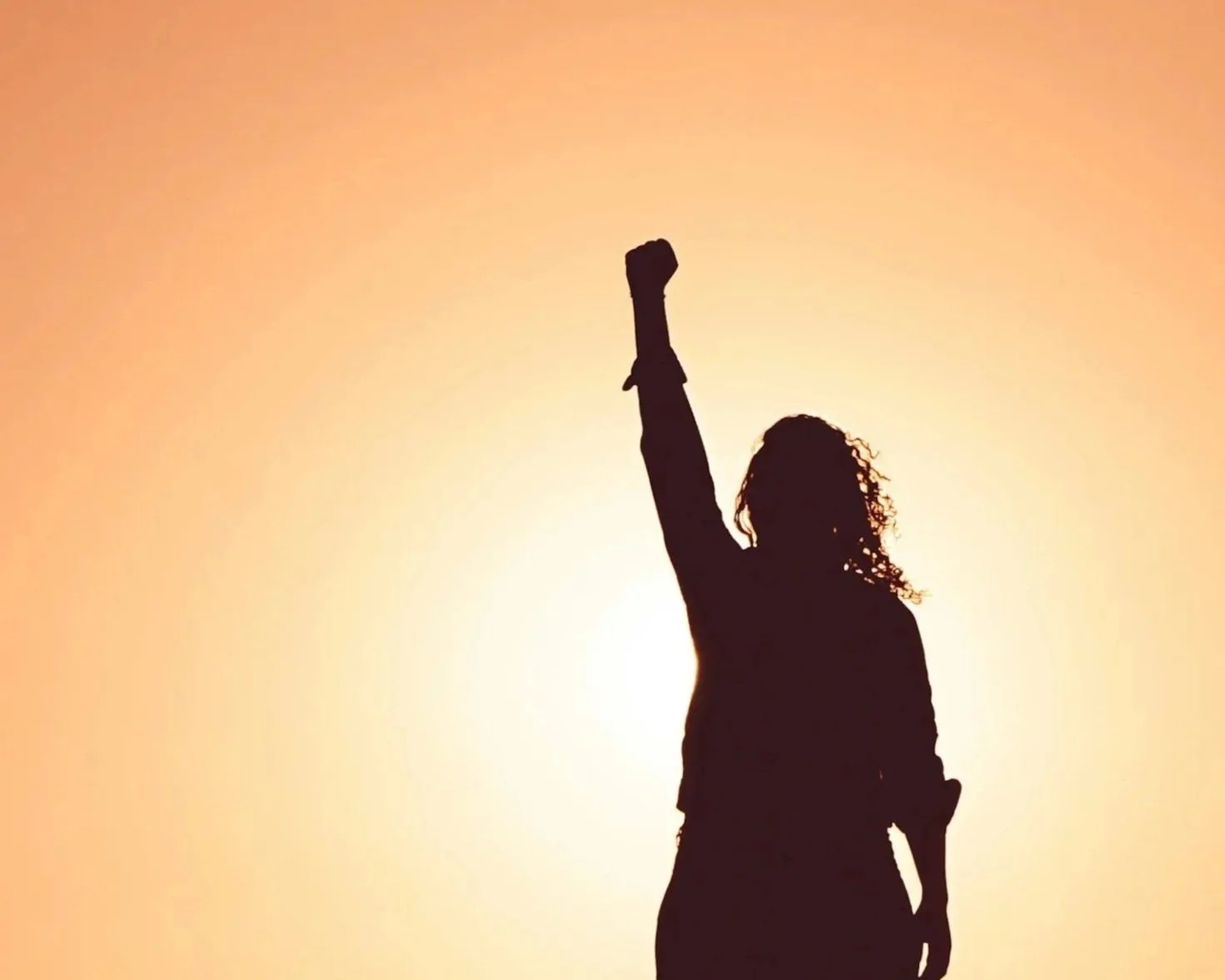 Silhouette d'une femme avec un bras levé contre un coucher de soleil.