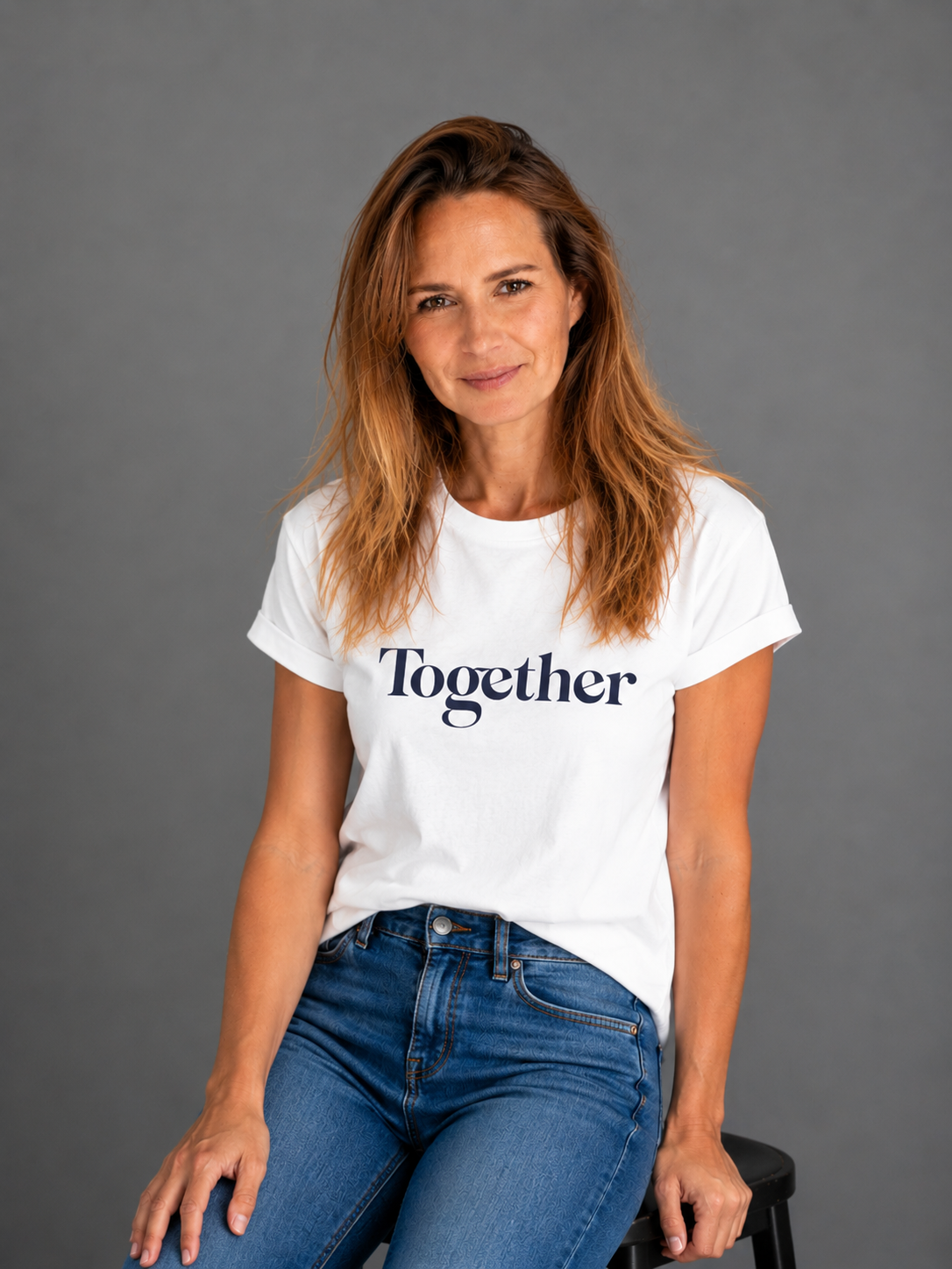 Femme assise portant un t-shirt blanc avec le mot 'Together' écrit dessus, contre un fond gris.