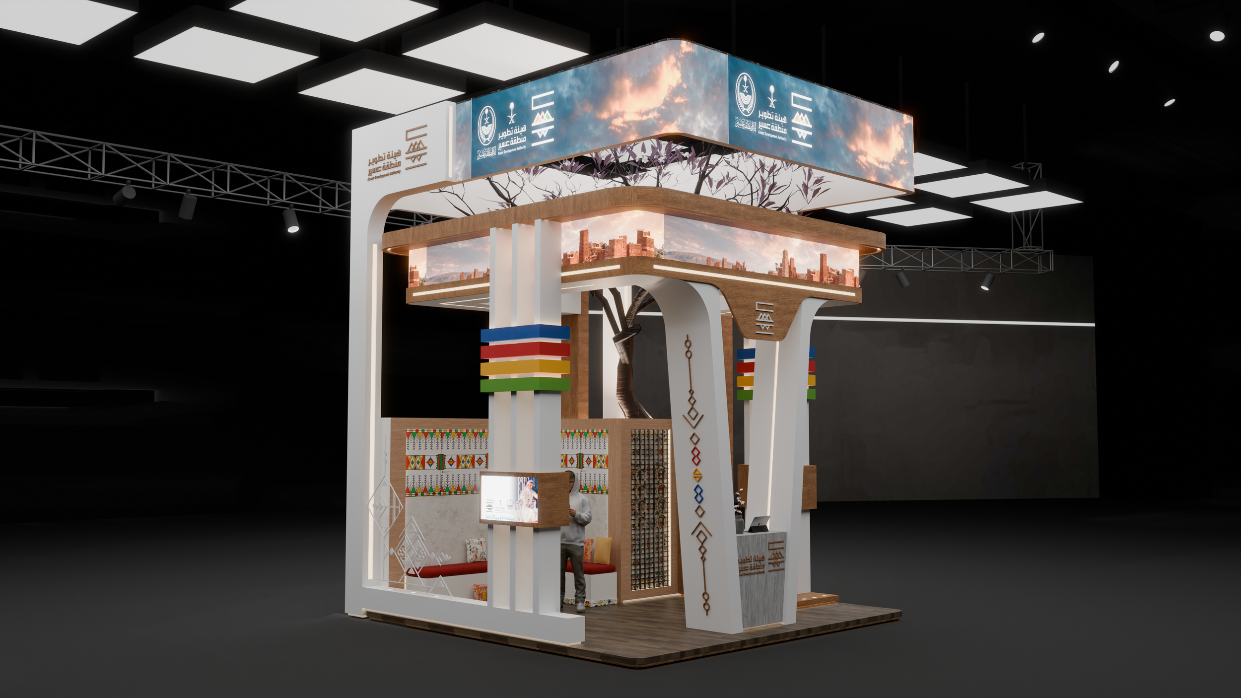 Exhibition booth featuring vibrant cultural decorations, digital screens, and signs with Arabic and English text, set in an indoor convention center with black ceiling and lighting.