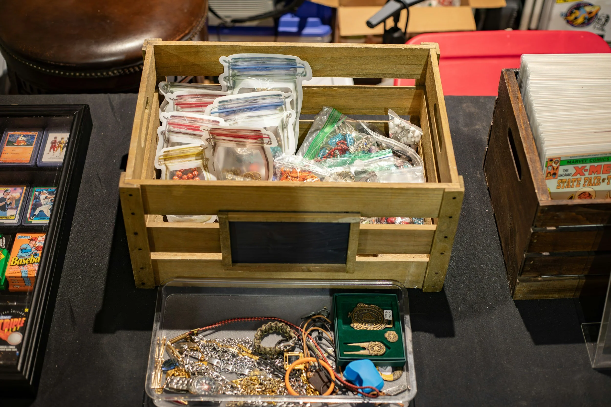 A wooden crate filled with various small memos or buttons, some in plastic ziplock bags, on a black table at a flea market or garage sale.
