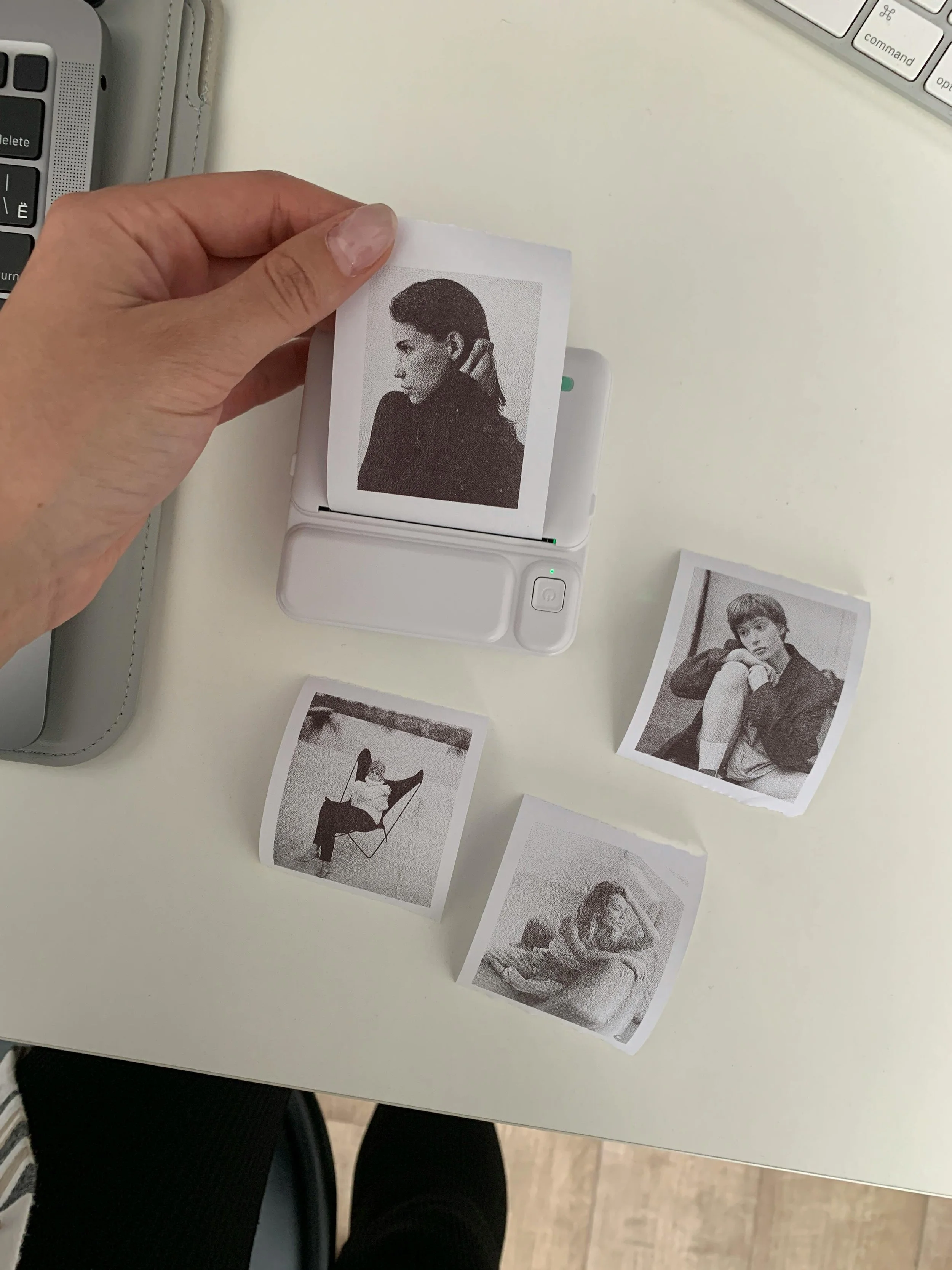 Black and white instant photos on a white table with a person's hand holding one photo and a small printer.
