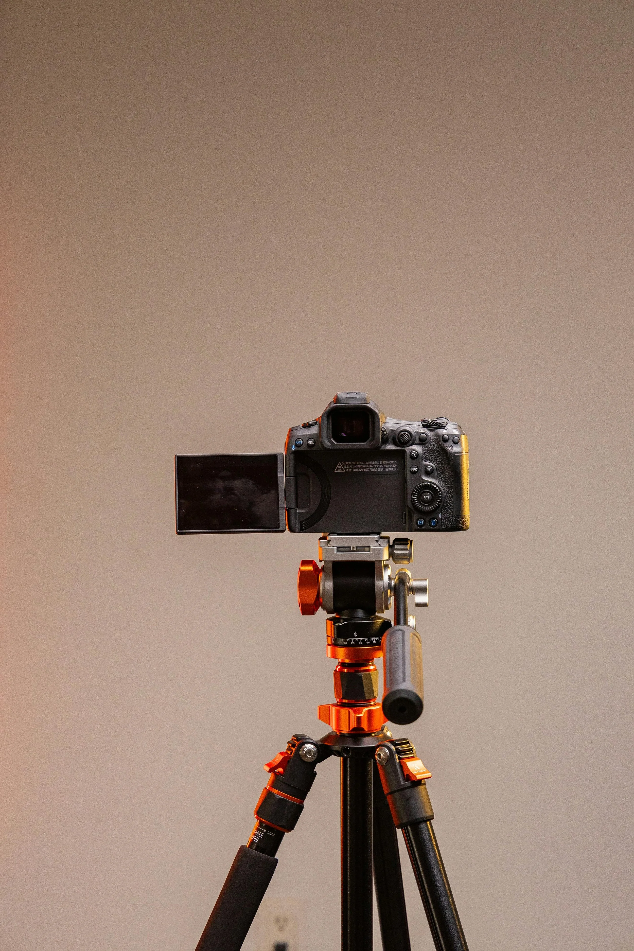 A professional camera mounted on a tripod, facing a neutral gray background.