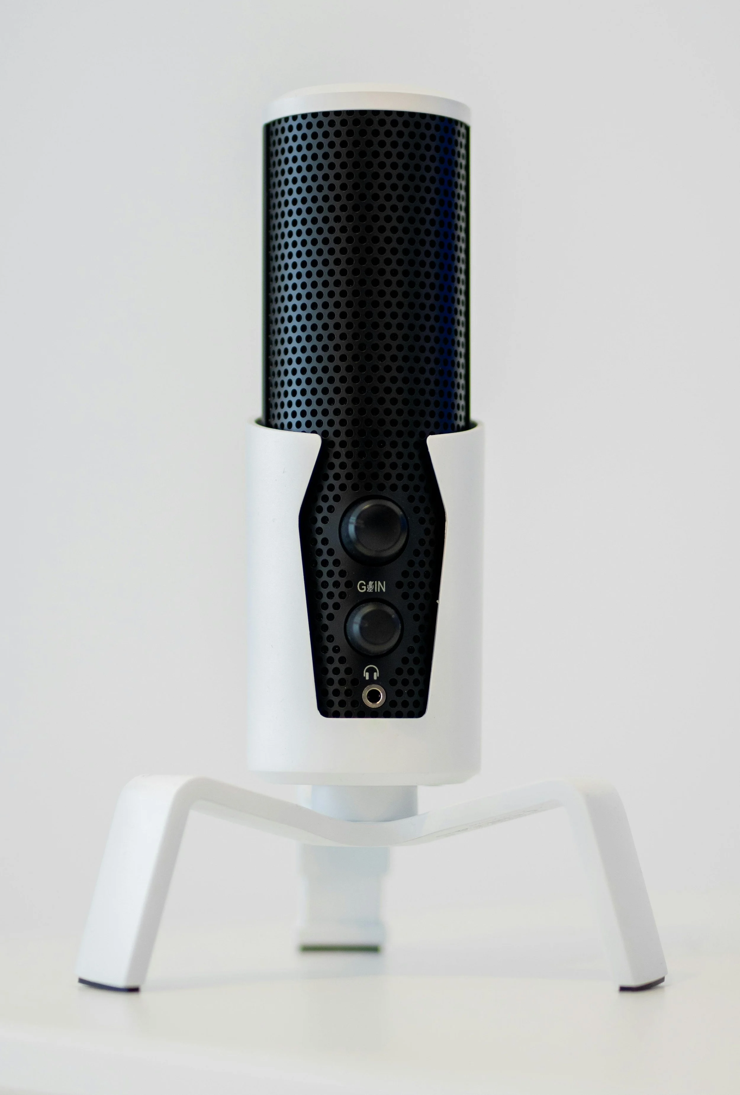 A white and black smart speaker on a white stand against a plain white background.