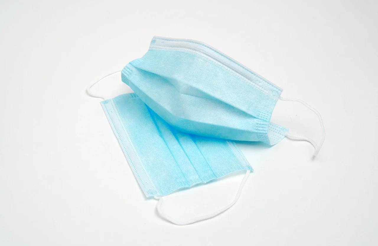 Two blue disposable face masks on a white surface, one mask partially folded.