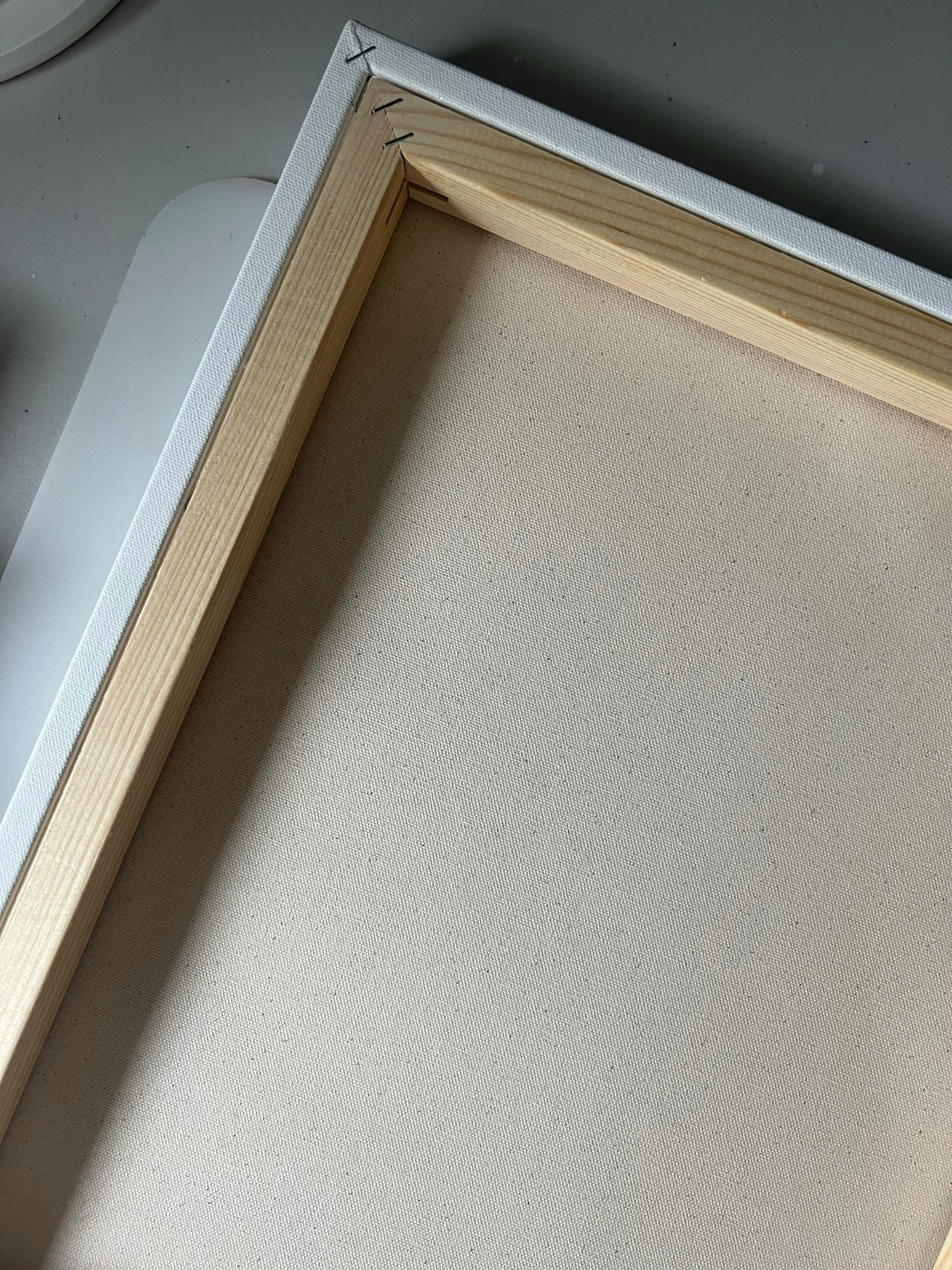 Backside of an blank canvas stretched on a wooden frame, with staples visible on one corner, lying on a table.