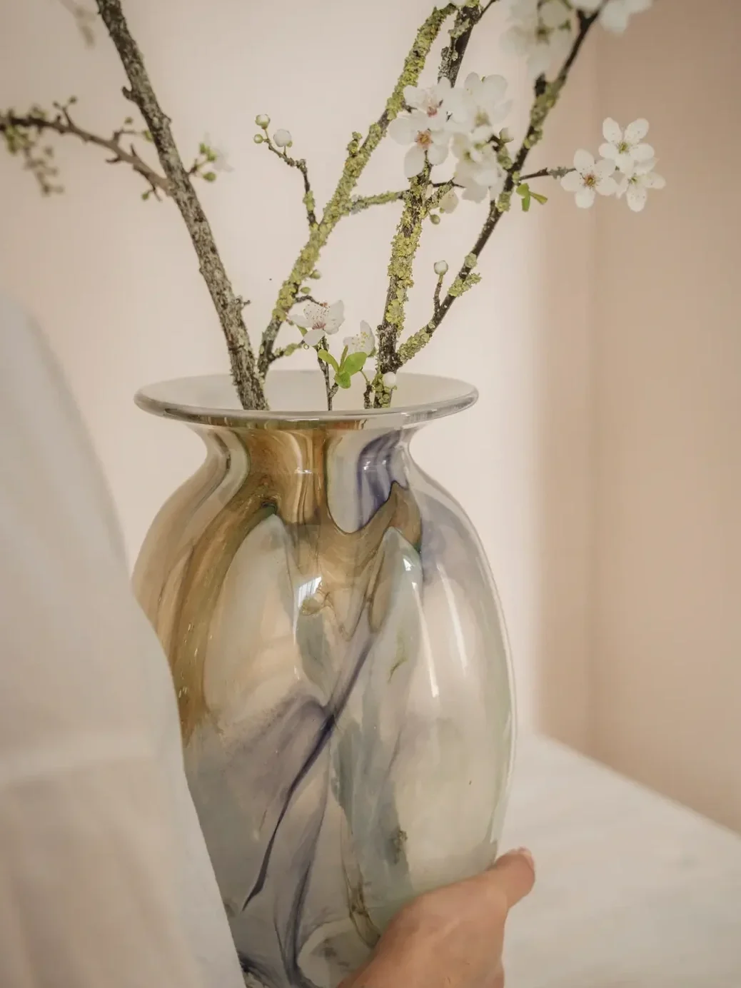 Vase en marbre contenant des branches d'arbustes avec de petites fleurs blanches