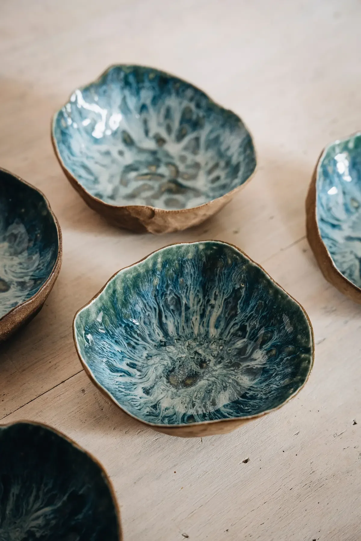 Petites coupelles en céramique avec intérieur à motif bleu et vert, disposées sur une surface en bois clair.