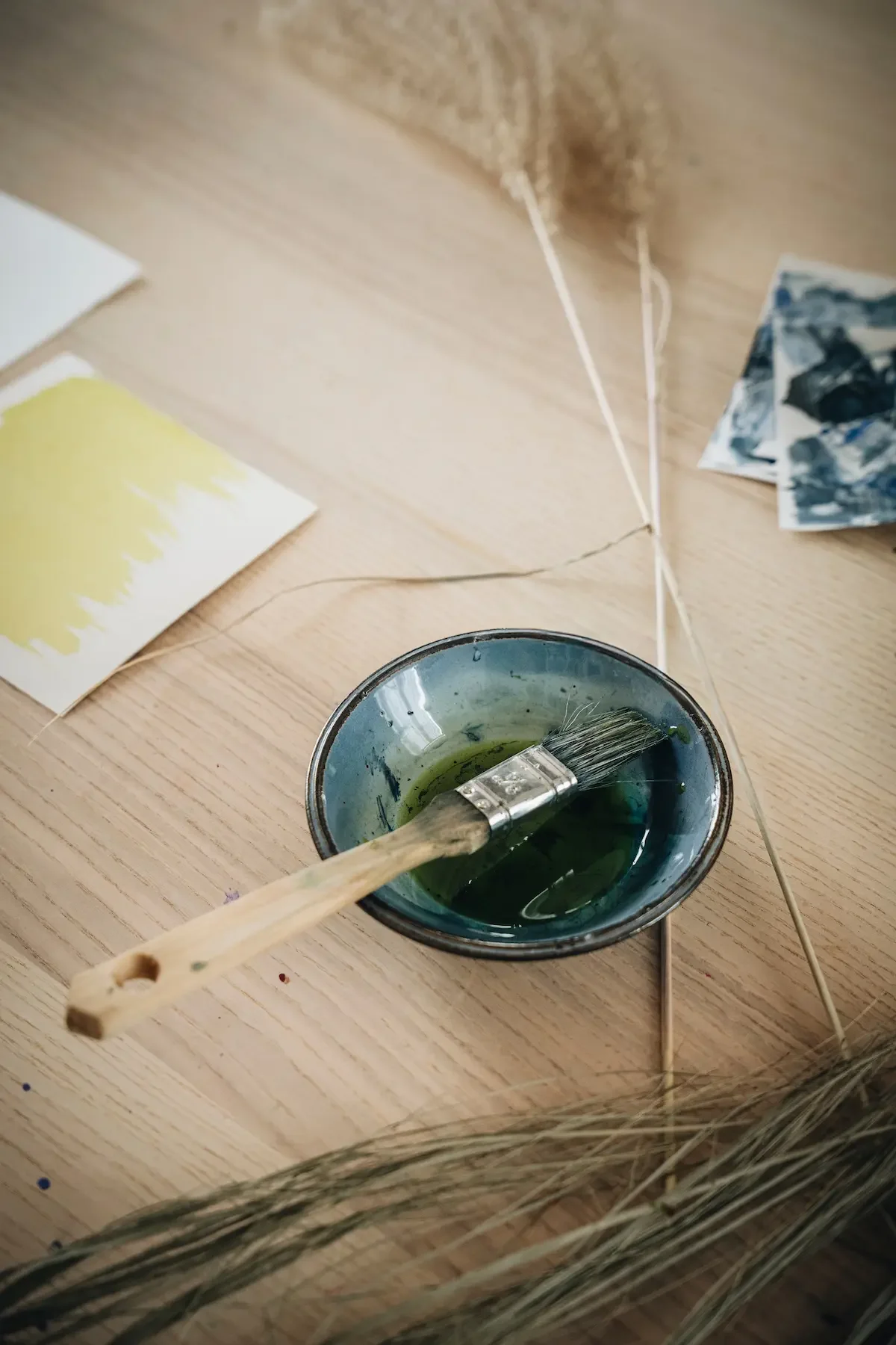 Fourniture pour la peinture, pinceau dans un bol de peinture verte, échantillons de couleurs et autres matériaux sur une table en bois.