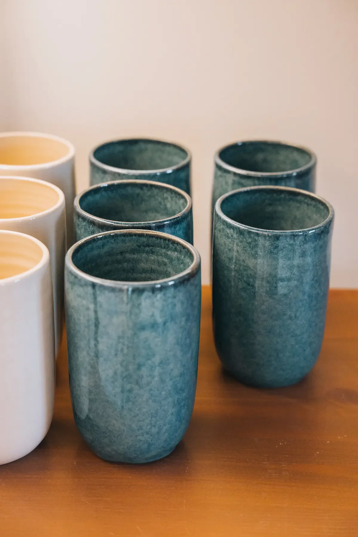 Gobelets en céramique, certains blancs, d'autres bleus, disposés en deux rangées sur une surface en bois.