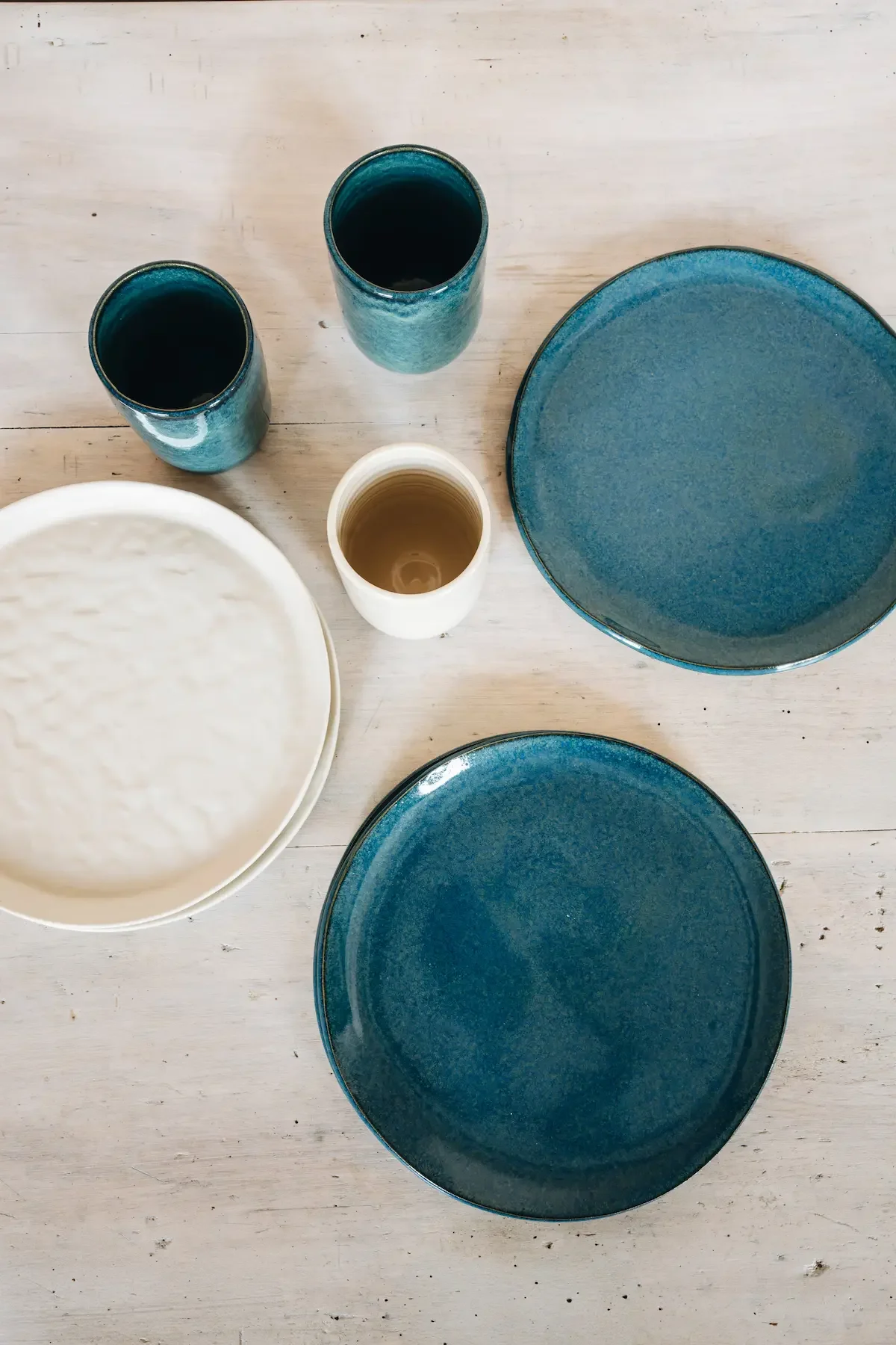 Vaisselle en céramique bleue et blanche sur une table en bois, comprenant deux grands assiettes, deux grands verres bleus, un petit verre blanc, et un bol blanc.