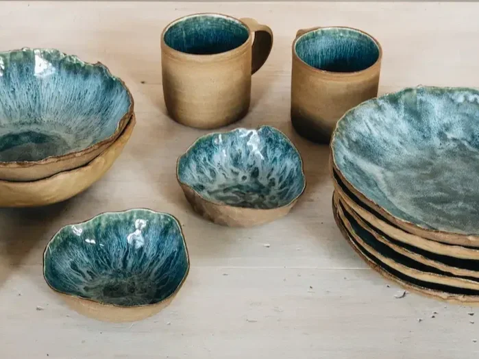 Assortiment de vaisselle en céramique avec intérieur bleu et extérieur beige, comprenant des bols et des mugs, sur une surface en bois.
