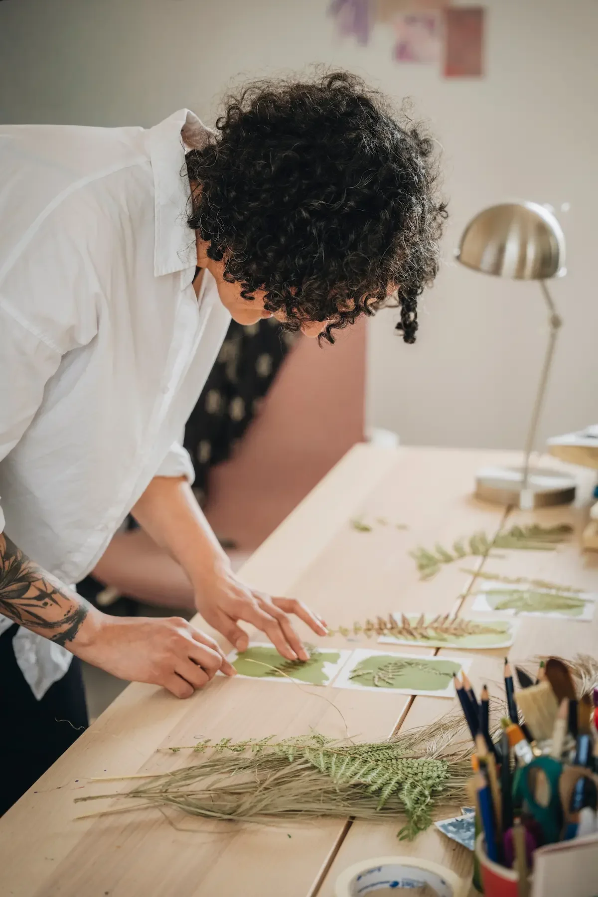 Une femme avec des tatouages crée des œuvres d'art avec des feuilles et des branches sur une table en bois.