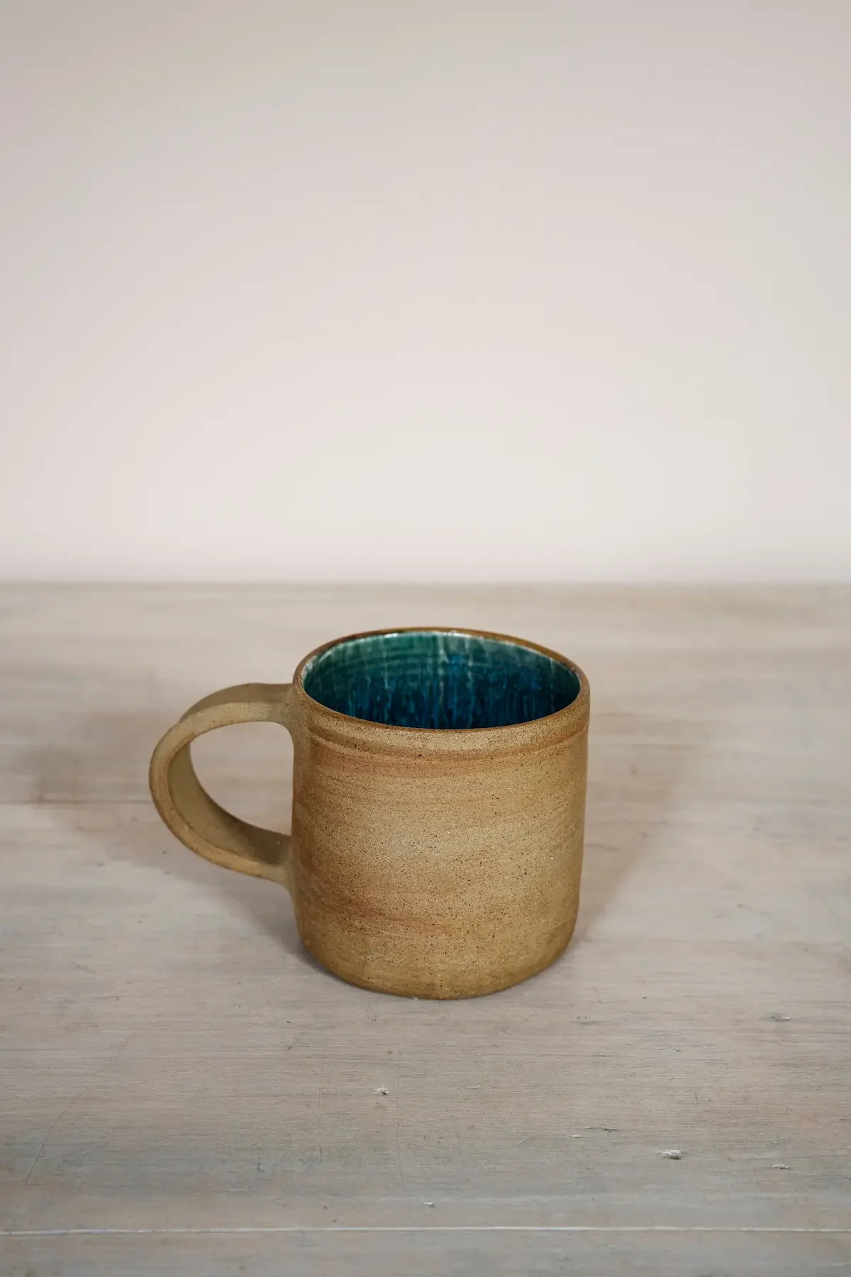 Tasse en céramique beige avec intérieur bleu foncé, placée sur une surface en bois clair.