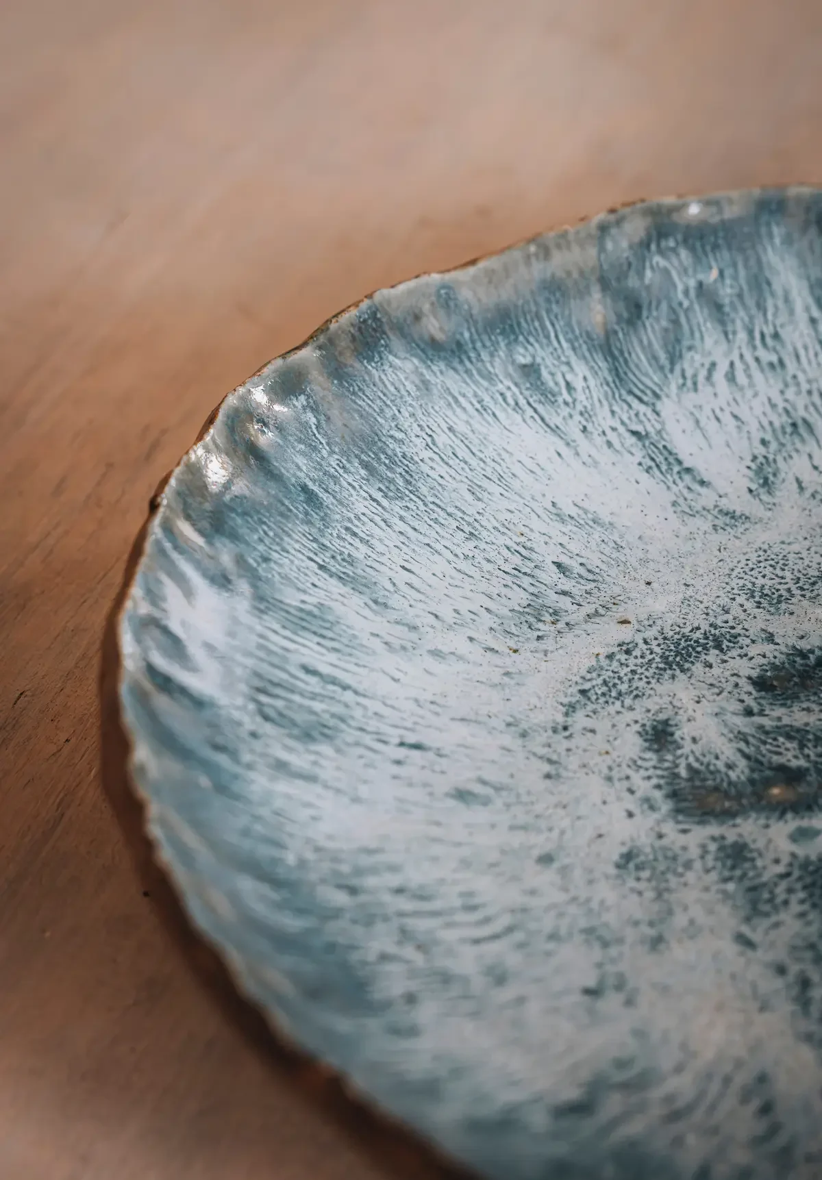 Un plat en céramique bleu-vert avec une texture ondulée et un design artistique, posé sur une surface en bois