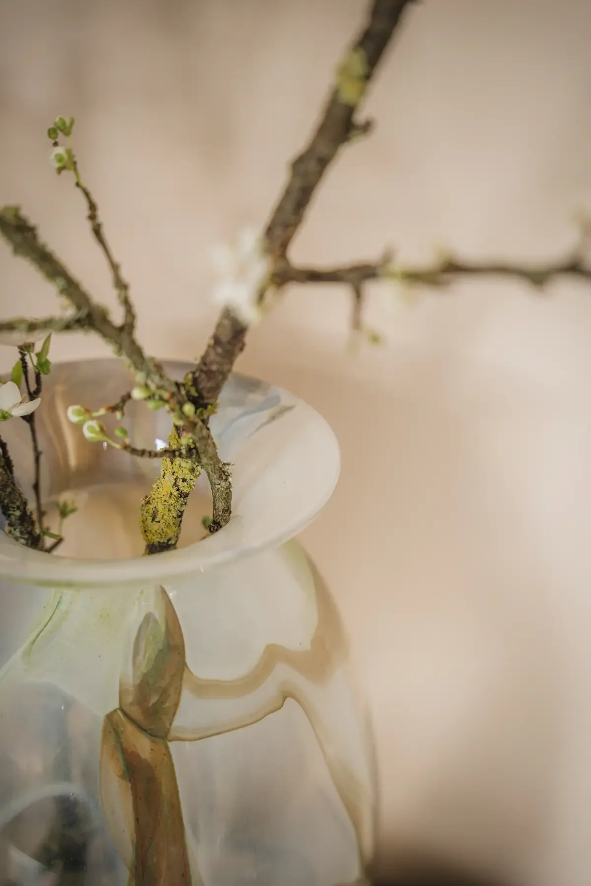 Branches d'arbre dans un vase en céramique avec une finition émaillée irisée beige et blanche.