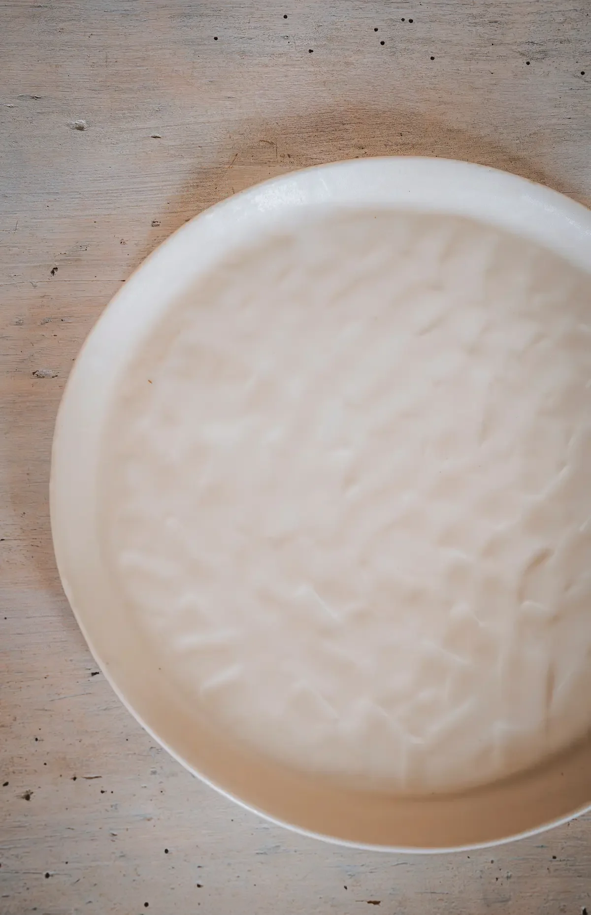Plat rond blanc avec une texture douce, posé sur une surface en bois clair.