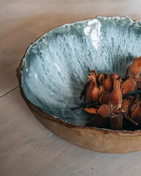 Un bol en céramique avec un intérieur bleu et des graines d'ail séchées à l'intérieur, posé sur une surface en bois.