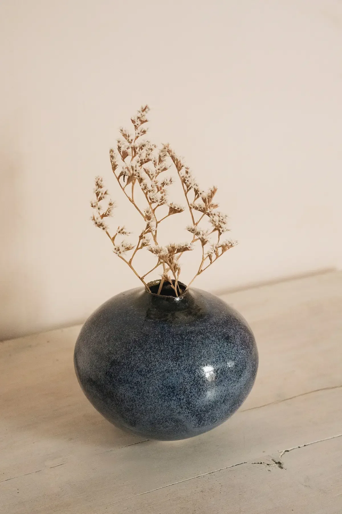Vase ronde en céramique noire avec rameaux secs blancs à l'intérieur, posé sur une surface en bois clair.
