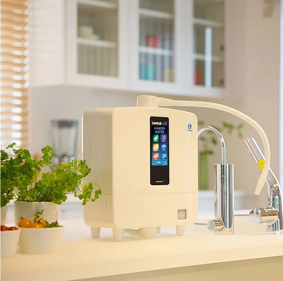 Enagic K8 Kangen water system on a kitchen counter next to a sink and a bunch of herbs.