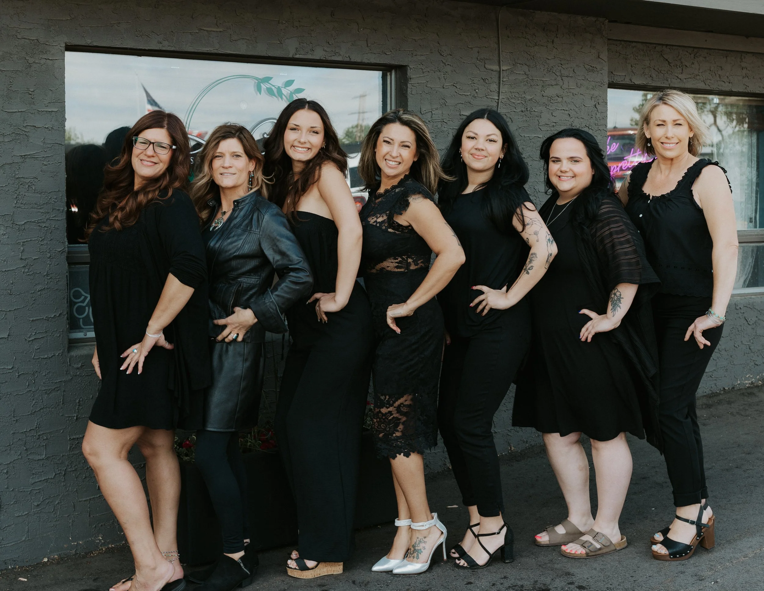 Group of eight women standing in front of a gray brick wall