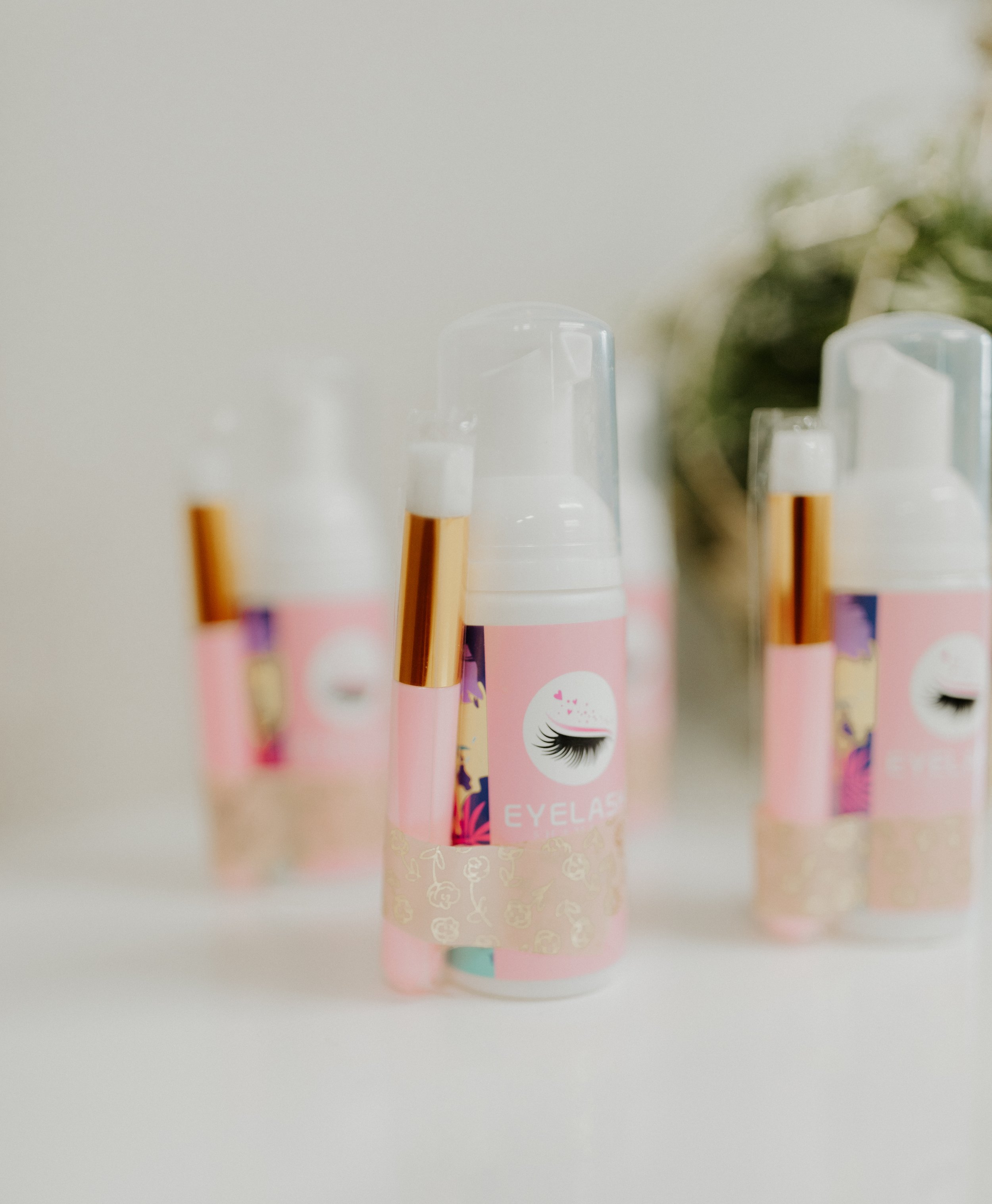 Bottles of eyelash extension adhesive with pink labels and gold accent details.