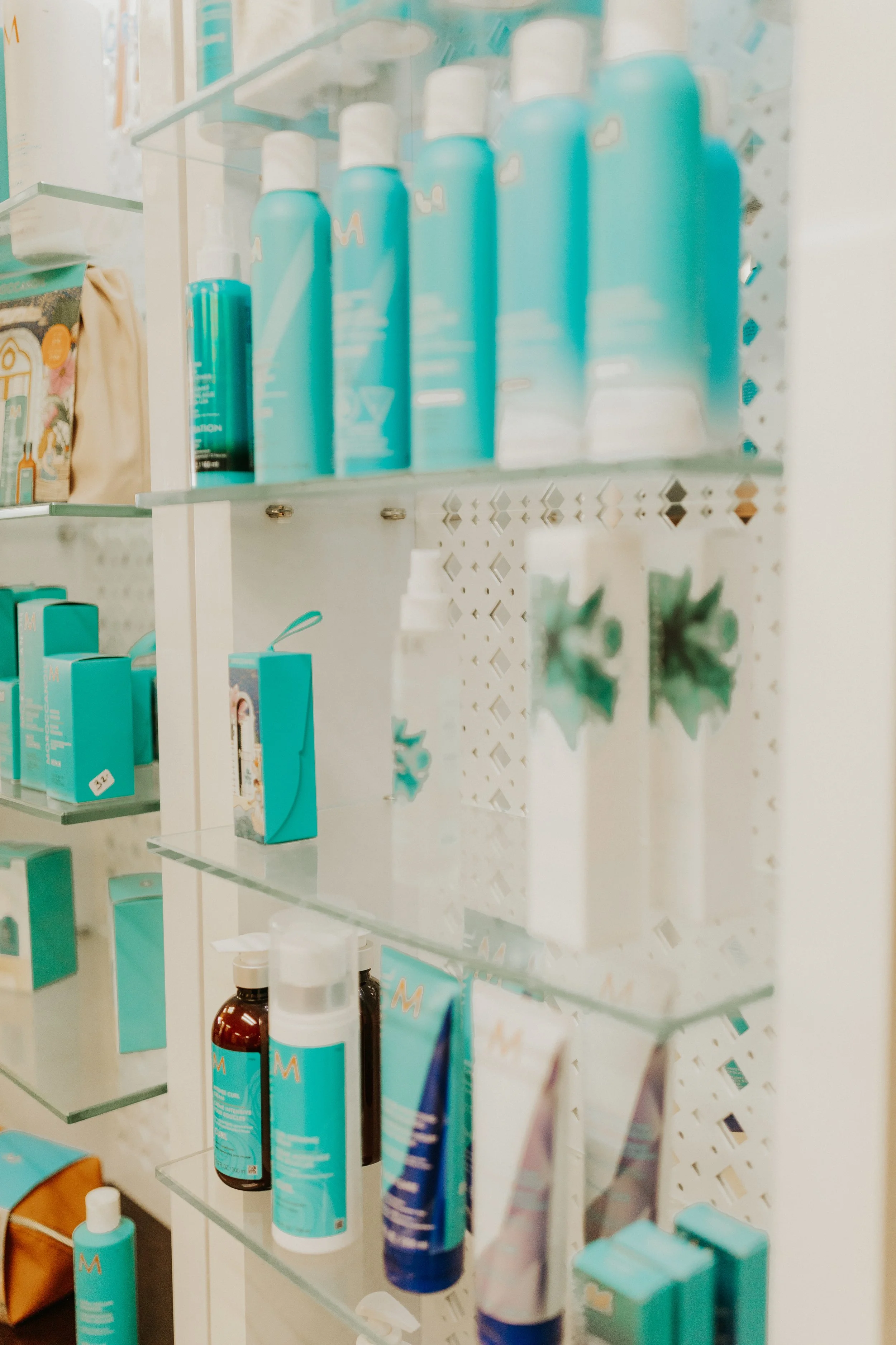 Shelves with various teal and white skincare products called moroccan oil including bottles, tubes, and boxes displayed in a retail setting.