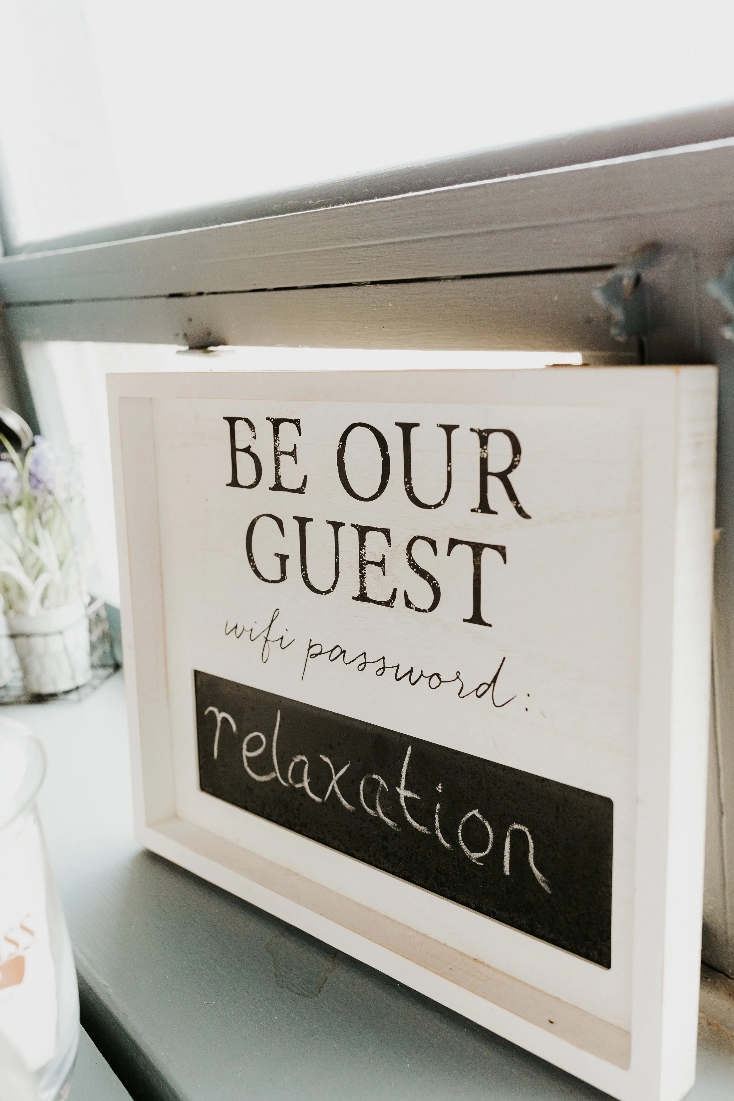 Decorative sign reading 'BE OUR GUEST' with a Wi-Fi password in handwritten script and a blackboard area labeled 'relaxation'.