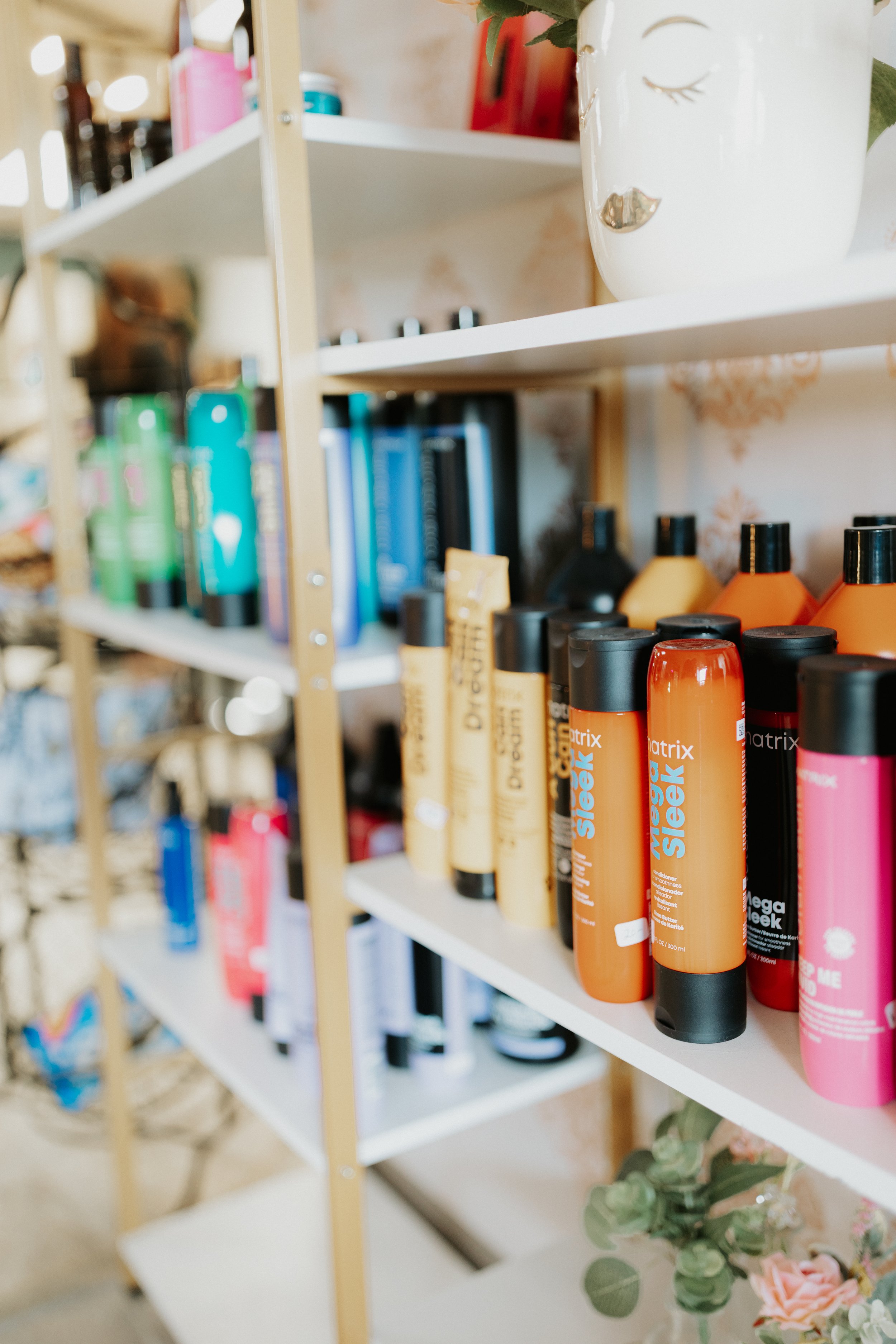Shelves with colorful hair care products and a decorative white vase with a face design.