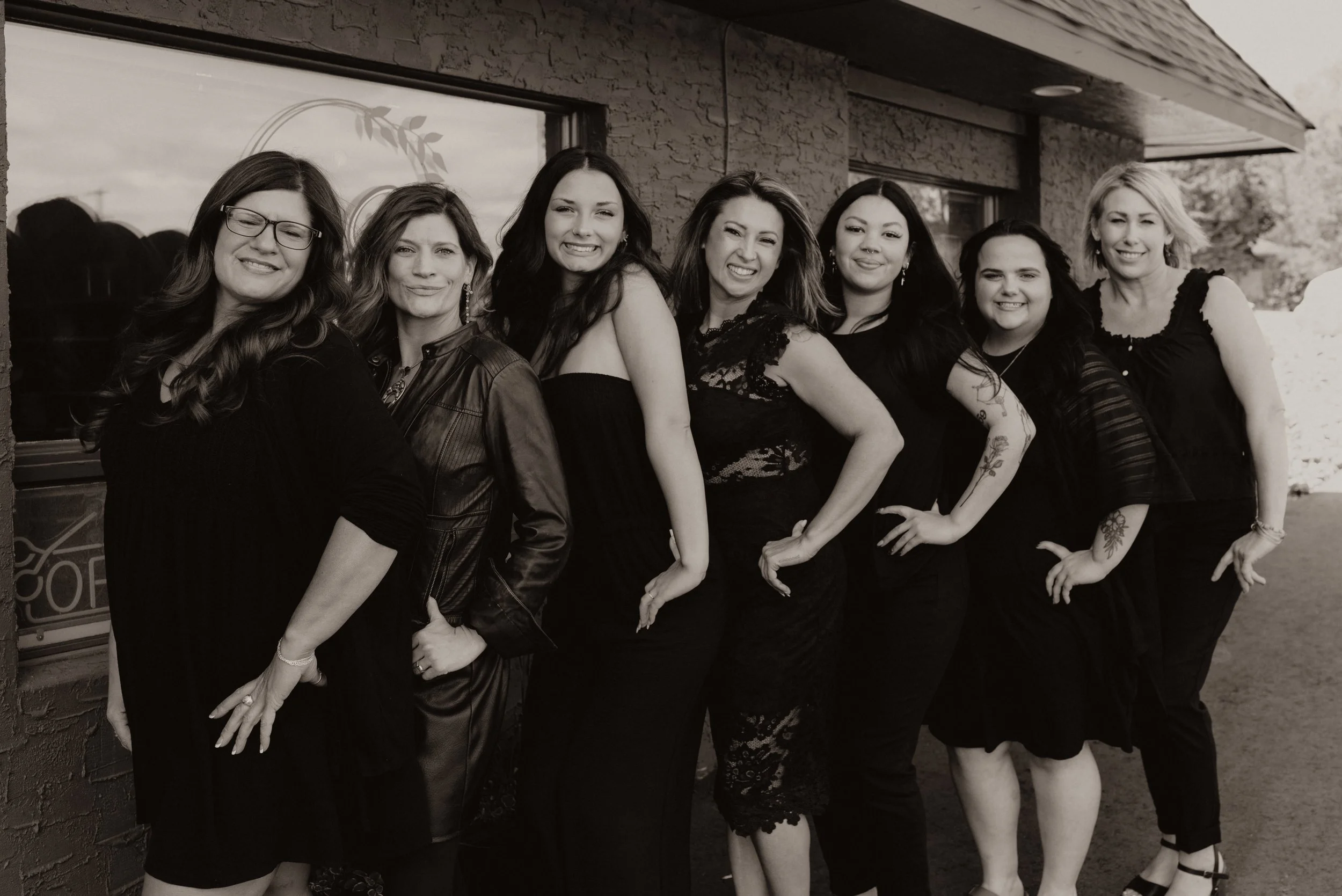 Seven salon stylists dressed in black standing outdoors in front of La Croix Salon and Spa, posing for a group photo.