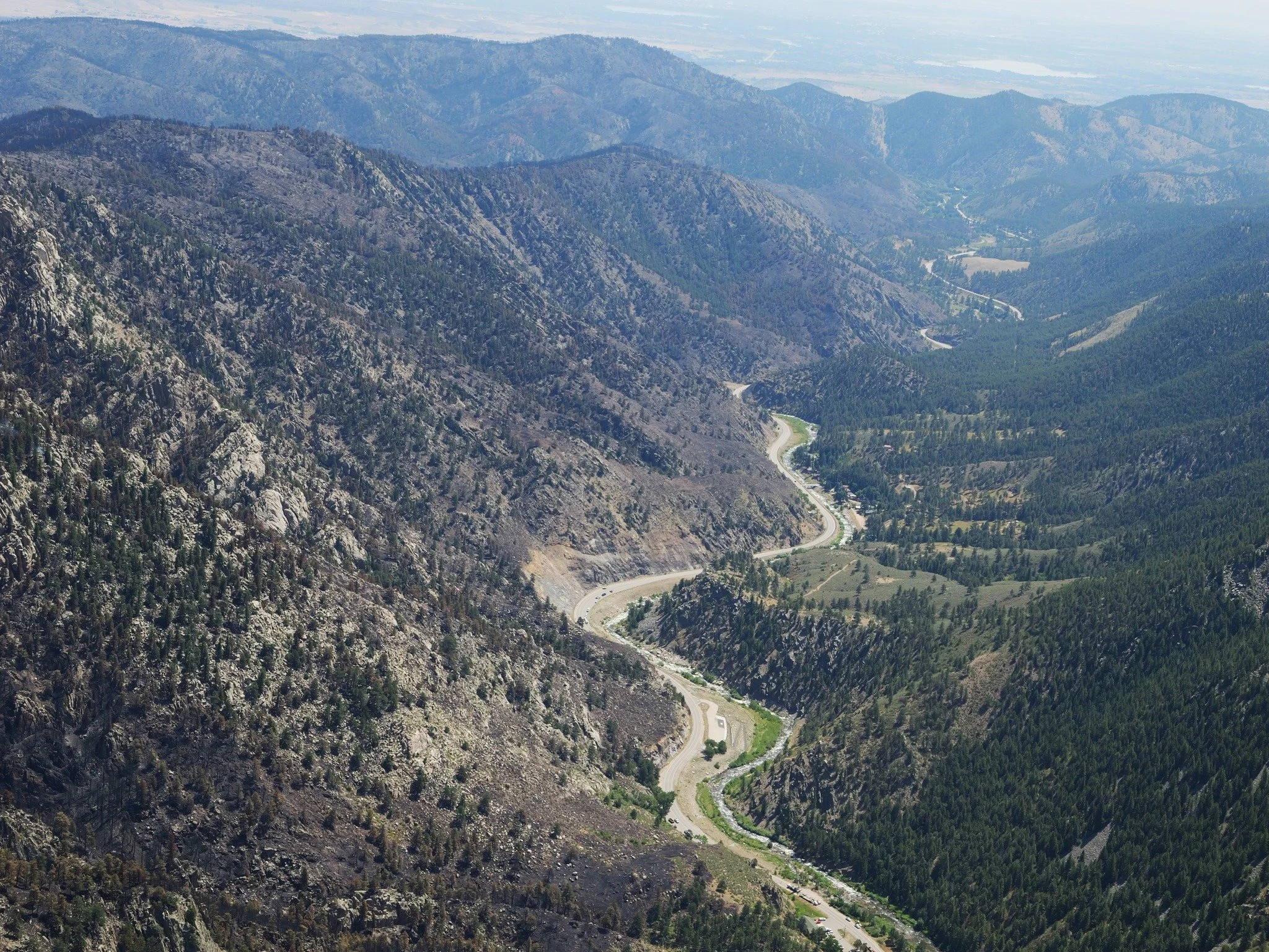 Aerial view of a mountain landscape with winding road and lush green forests.