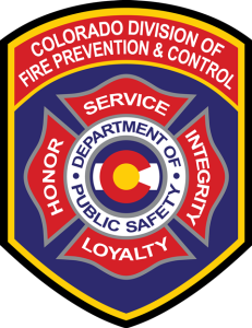 Emblem of the Colorado Division of Fire Prevention & Control featuring a firefighter badge design with 'Service' at the top, surrounded by words 'Honor', 'Loyalty', 'Integrity', and 'Public Safety'. The emblem includes the Colorado state flag colors.