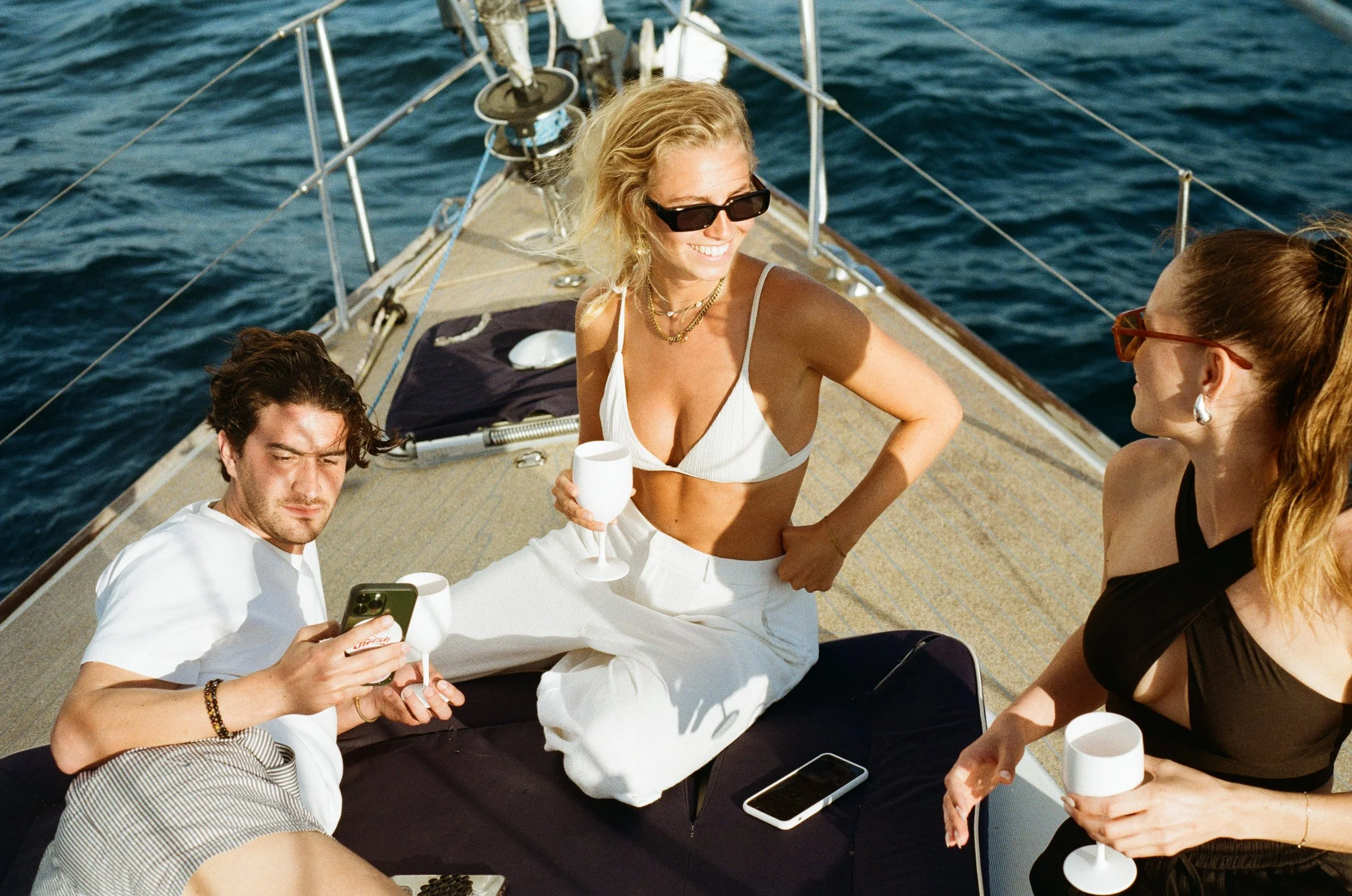 Three people relaxing on a yacht, holding drinks, with ocean in the background.