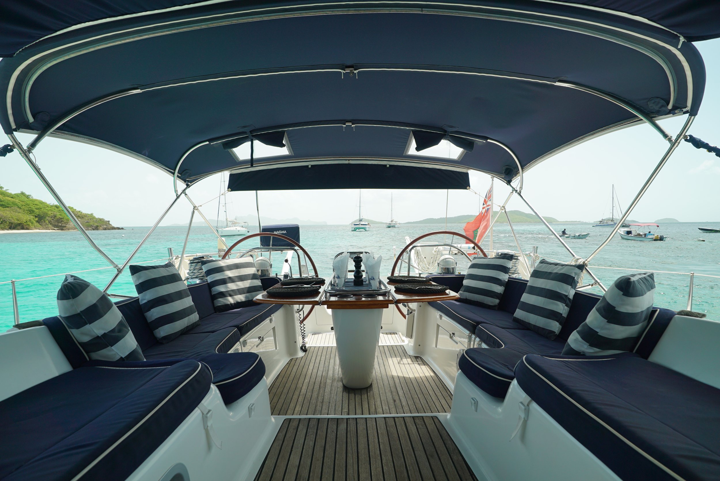 View of the deck on a yacht with outdoor seating, striped pillows, and a view of calm turquoise water with several other boats and a small island in the distance.