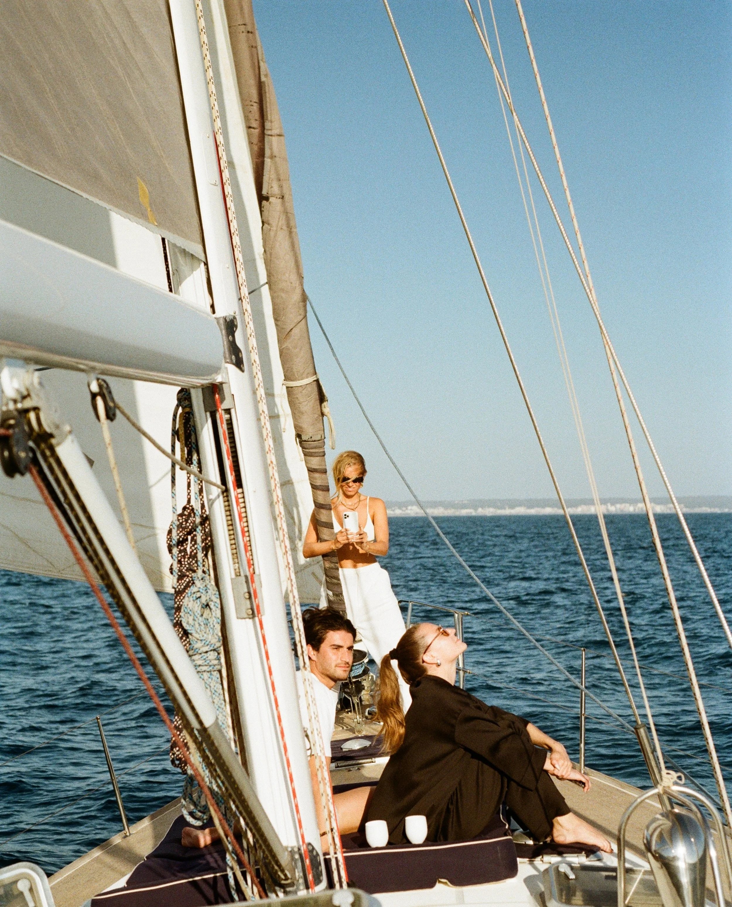 Four people on a sailboat in the ocean with a clear blue sky.
