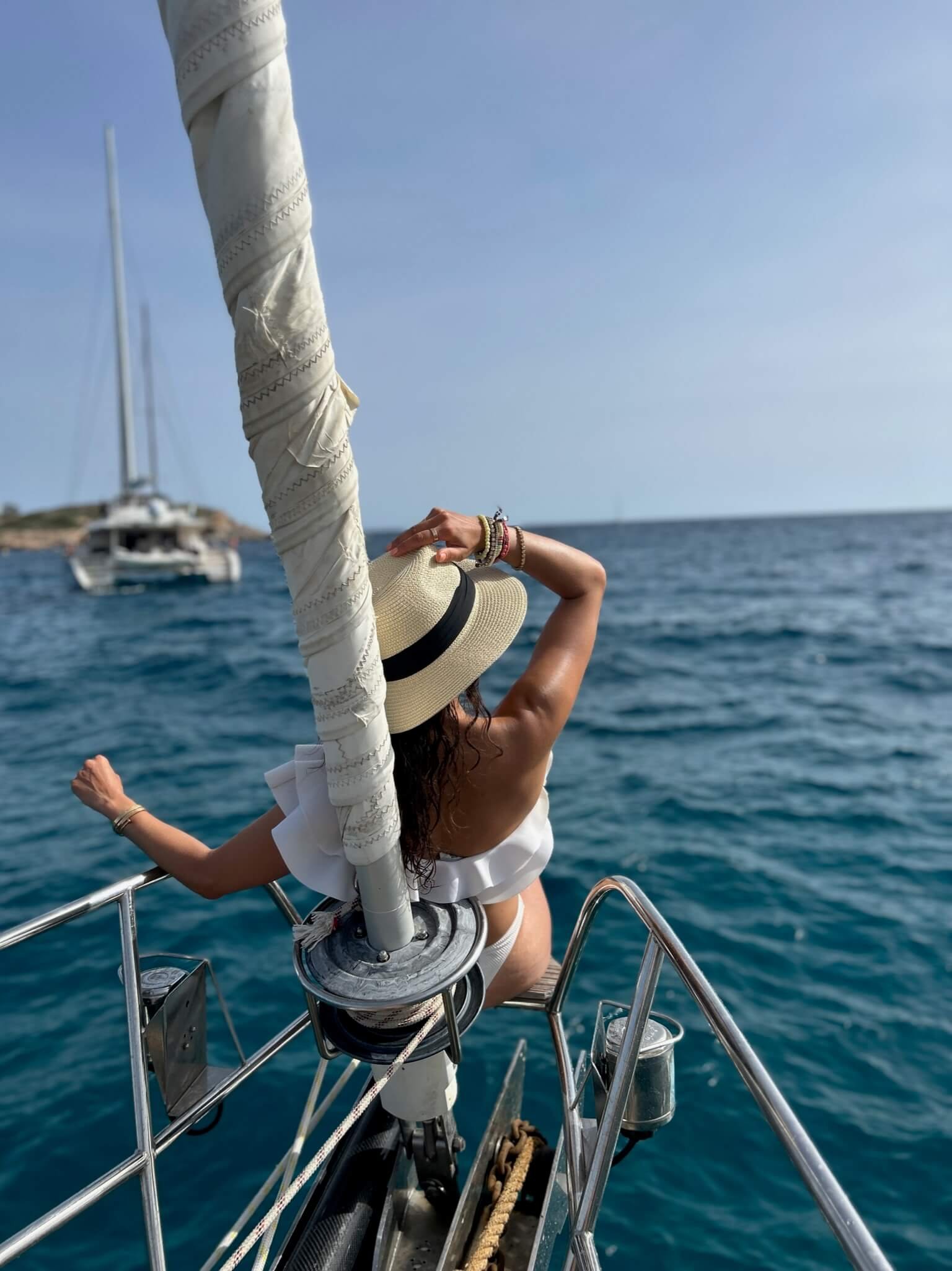 woman sitting on the the bowseat of a sailboat wearing a hat looking at the horizon