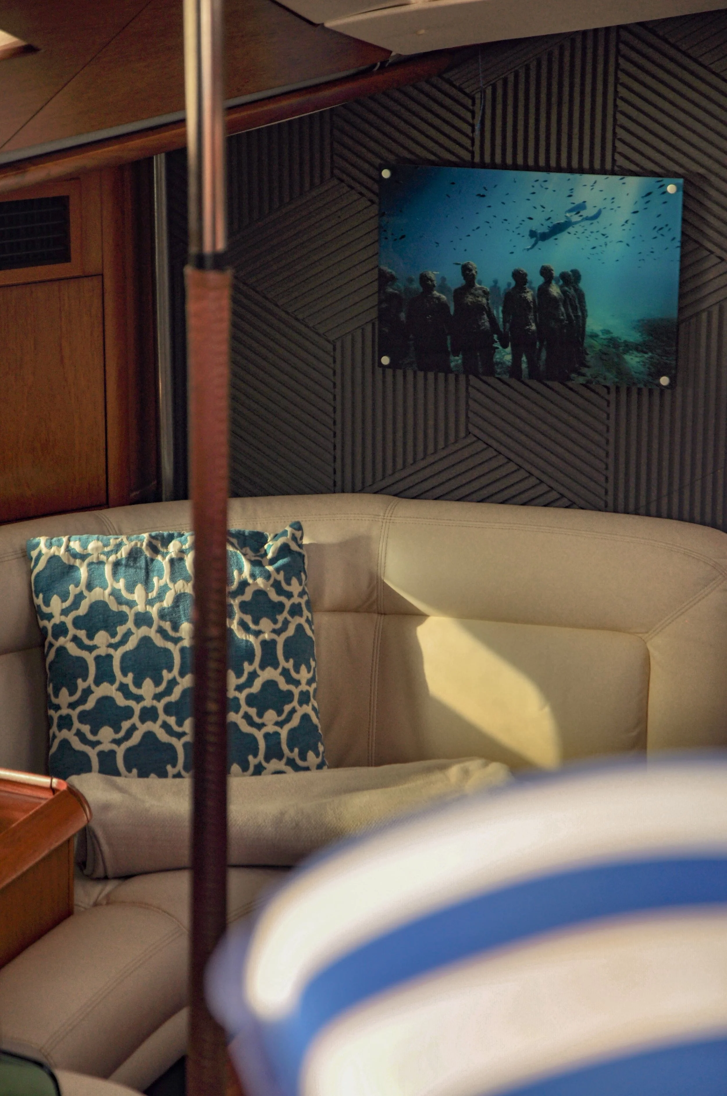 A beige sofa with a blue and white patterned throw pillow, in a room with wood-paneled walls and a framed underwater photograph of people and a diver.