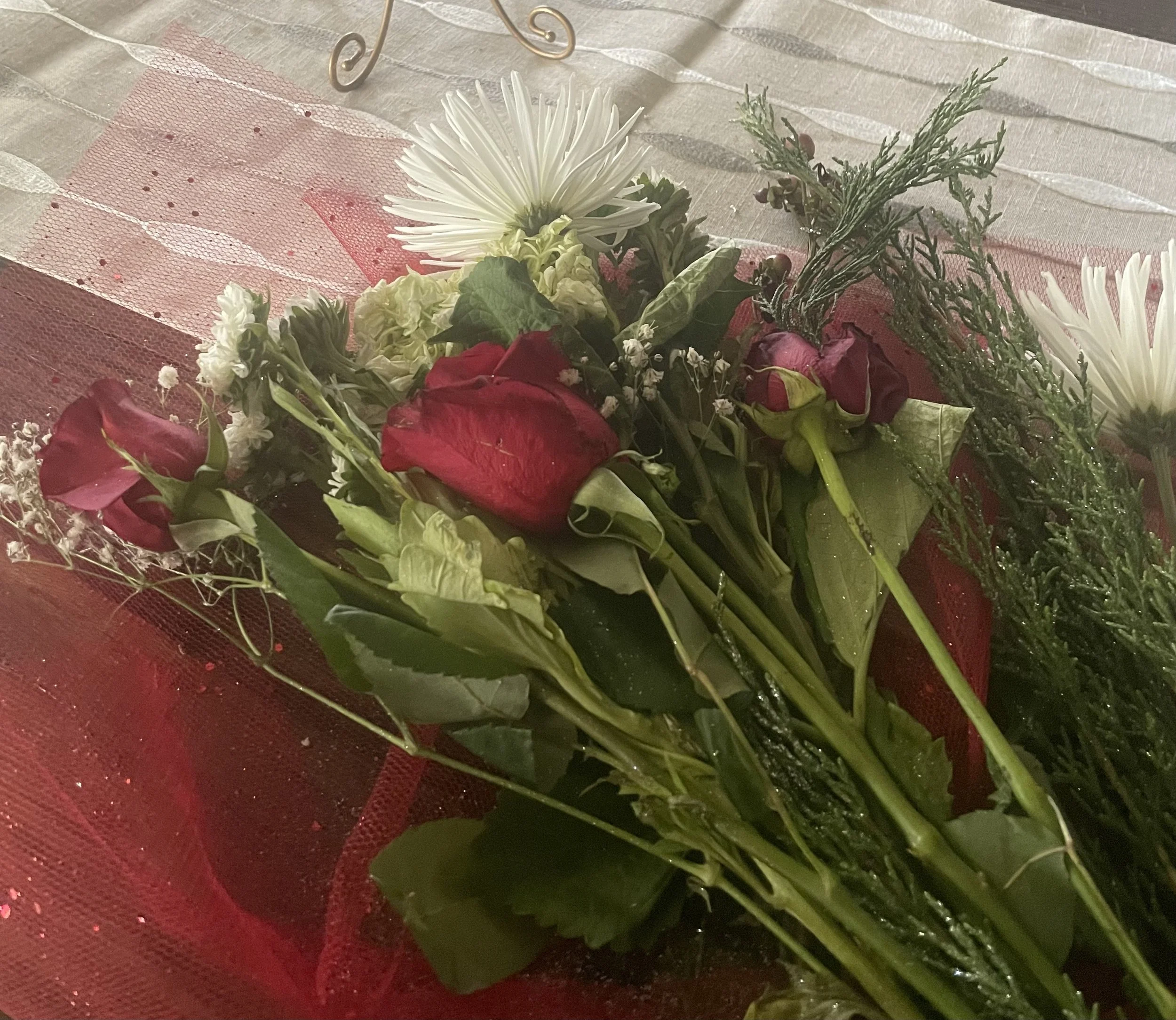 Arrangement of white, red, and green flowers on a decorative red and pink mesh backdrop.