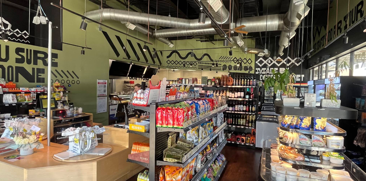 CraftFood Interior with shelves stocked with snacks, drinks, and pre-packaged food, a display case with fresh sushi, and a counter with a cash register.