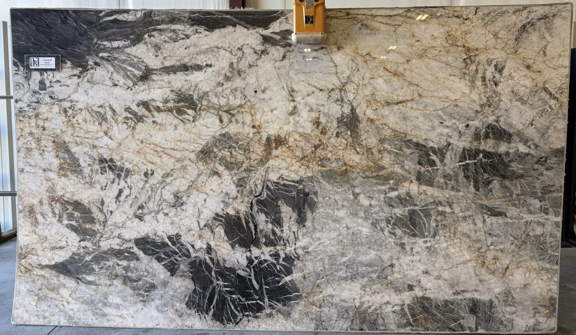 Large slab of marble with a mix of white, black, and beige veins, labeled "Crystal Noir" in the top left corner.