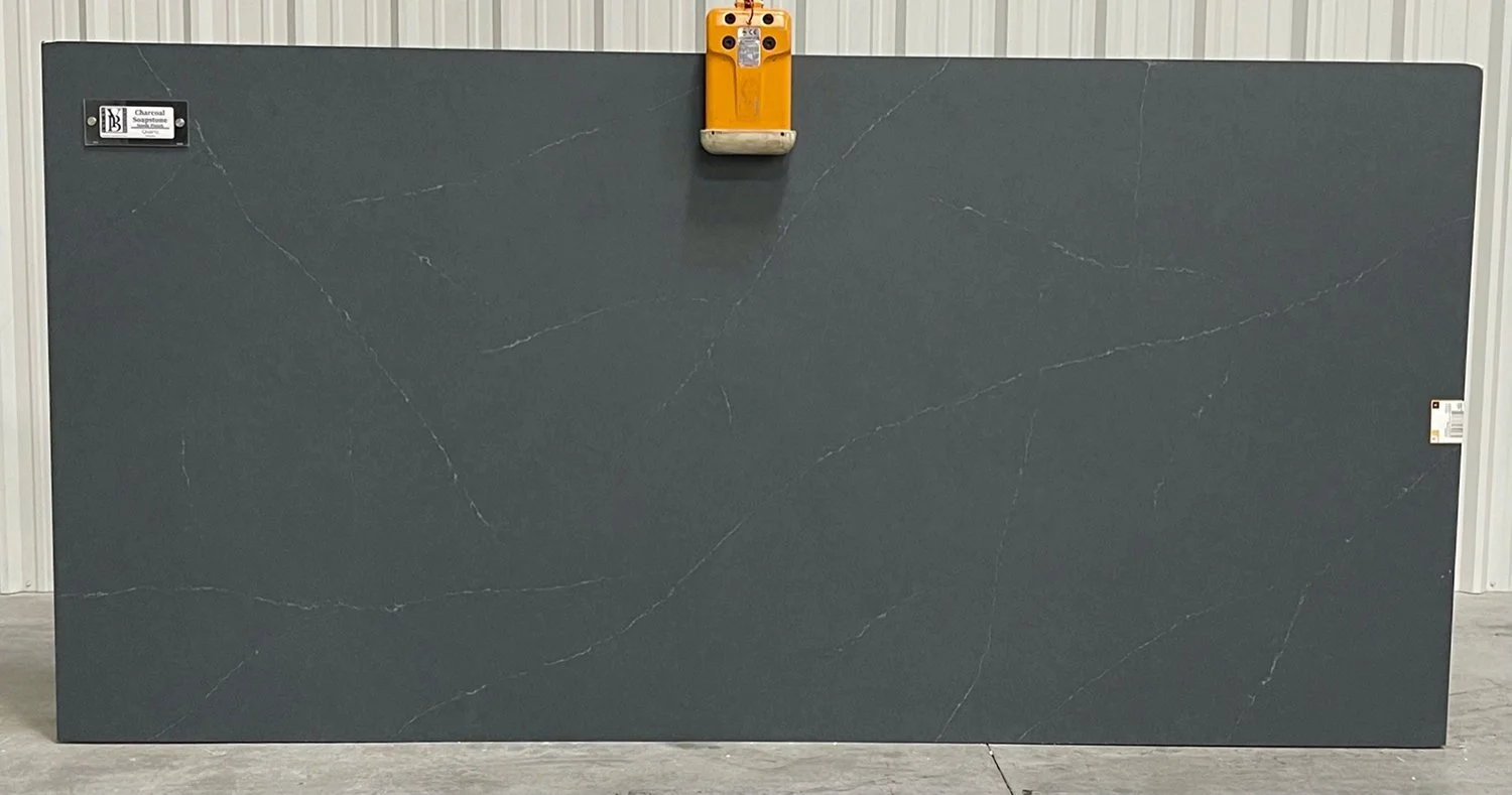 Large dark gray marble slab with white veining, standing upright against a white wall.