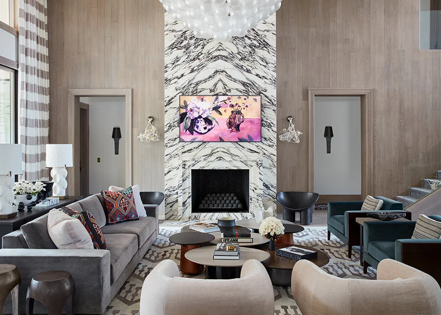 A modern living room with a marble fireplace, colorful pillows, contemporary furniture, and a large chandelier on the ceiling.