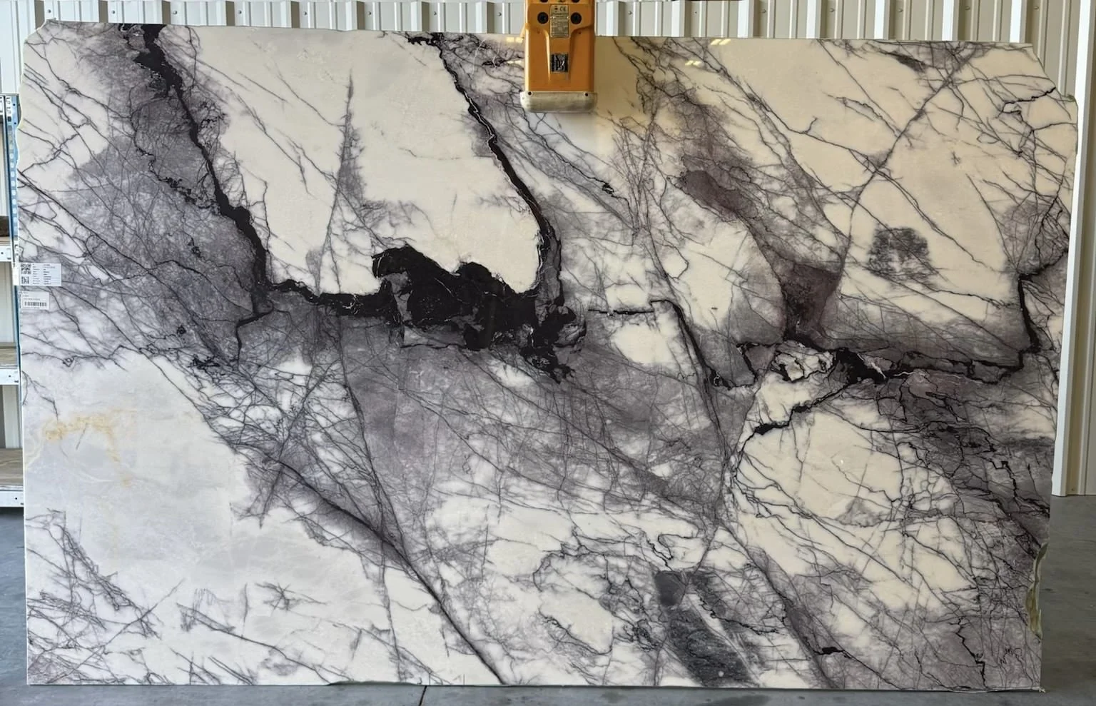 Large slab of white marble with black and gray vein patterns displayed on a stand in a warehouse.