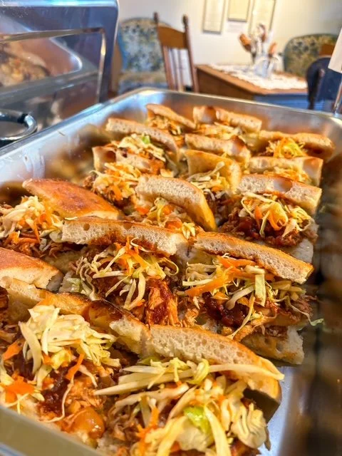 A tray of sandwiches filled with shredded lettuce, cheese, and meat, with some appearing toasted.