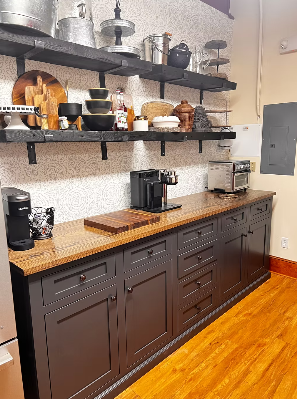 Kitchen with dark gray cabinets and a wooden countertop, open shelves with kitchenware, a coffee maker, and a toaster oven.