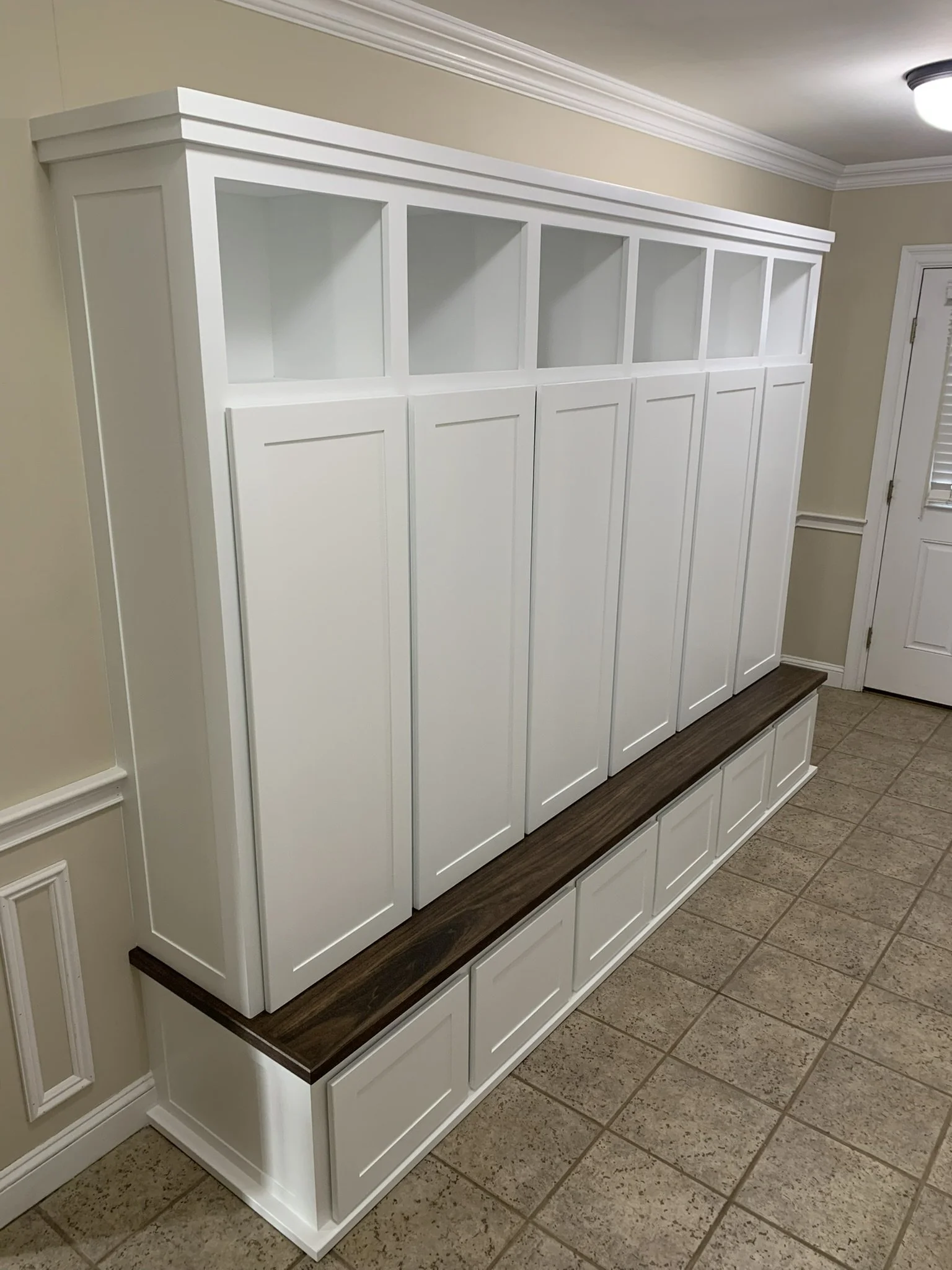 White built-in shelves and cabinets with a dark wood top in a room with beige walls and tiled floor.