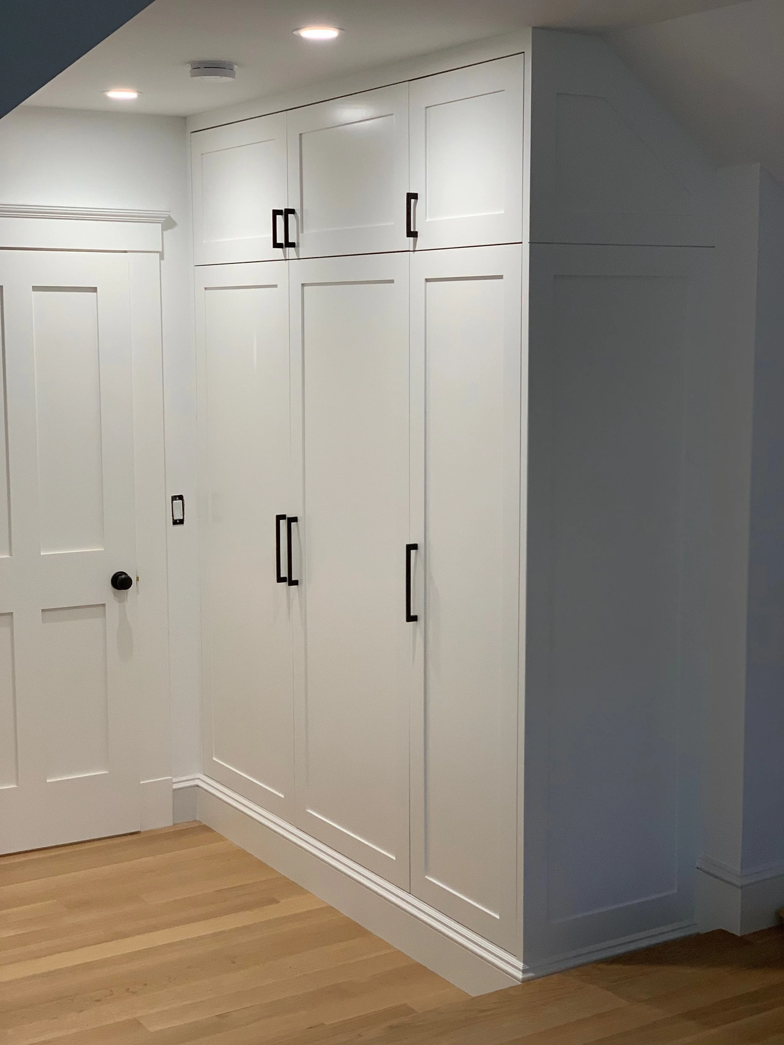 White built-in cabinets with black handles in a room with light wood flooring and white walls.