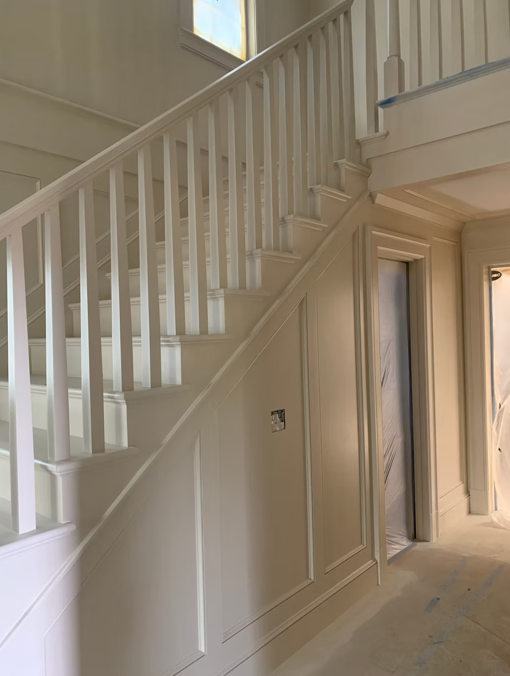 Interior view of a staircase with white balusters and wainscoting, under construction or renovation, with taped edges and an open doorway.